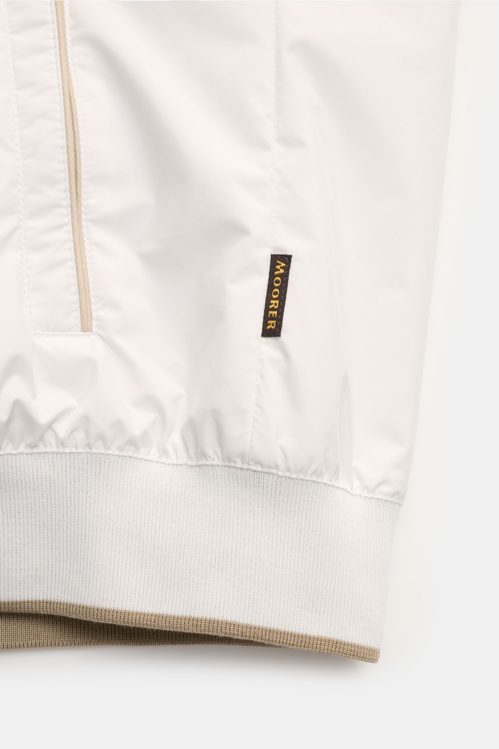 Close-up front view of the offwhite and beige Moorer Wende-Blouson 'Dennys' showing smooth microfiber, elastic hem, zipper pocket, and brand label.