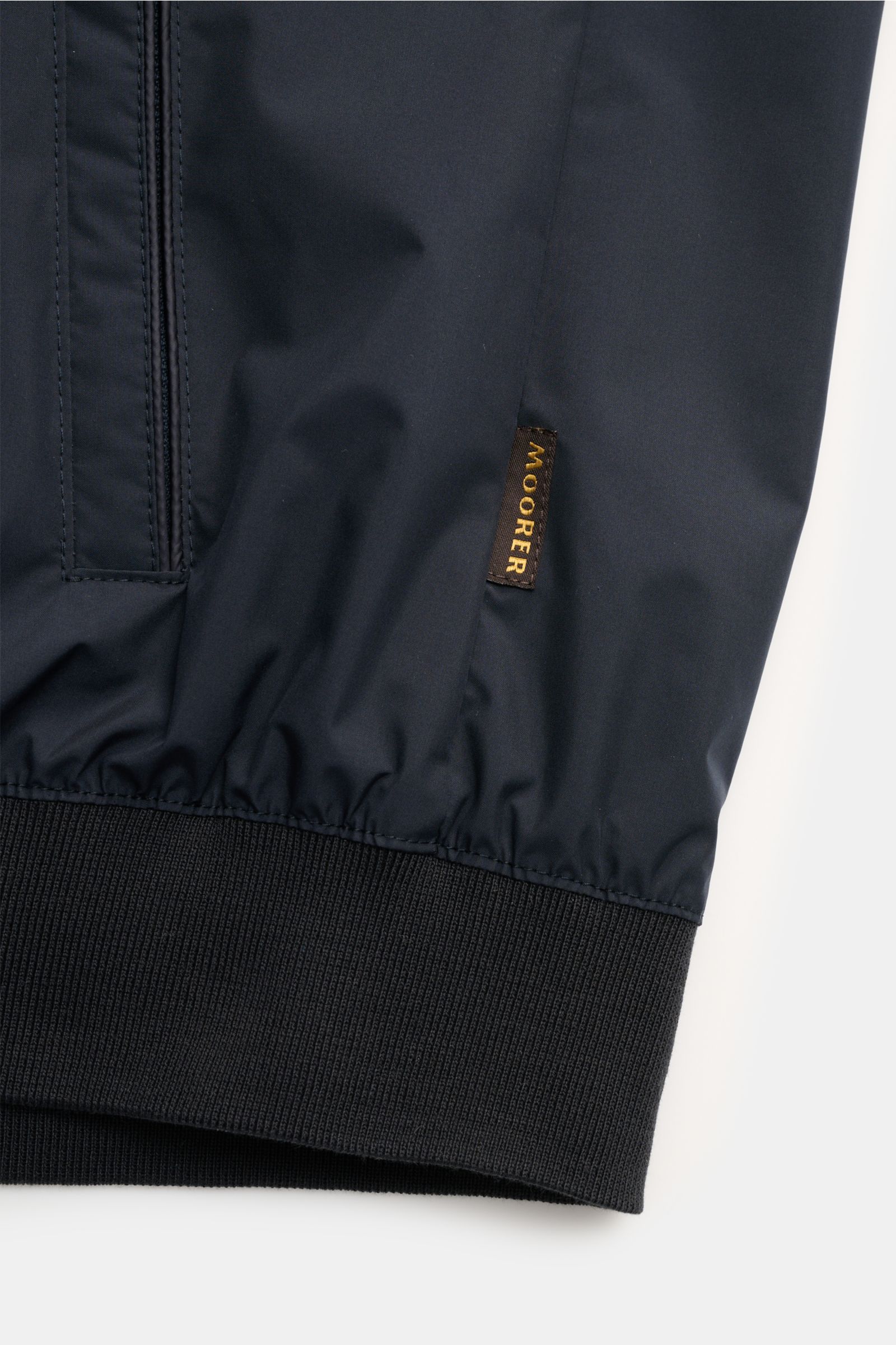 Close-up view of the ribbed hem and side pocket with Moorer label on the navy Moorer Wende-Blouson 'Dennys', made of smooth, water-repellent microfiber with elastic cuffs.
