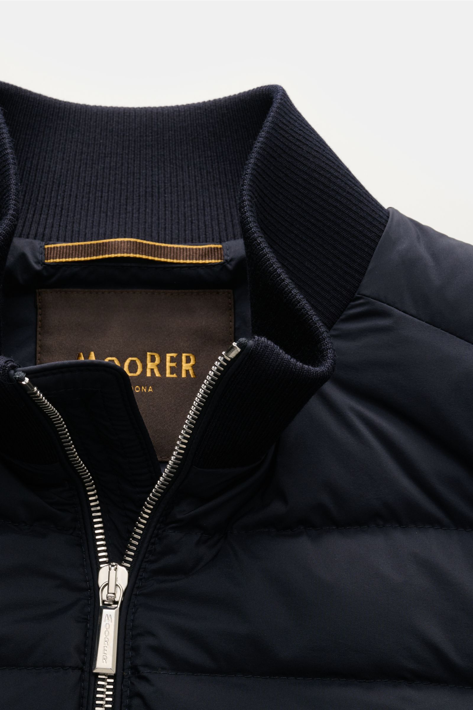 Nahaufnahme der Moorer Daunen-Strickjacke 'Duncan' navy, Front mit leichter Daunenfüllung, Stehkragen aus Rippstrick und silbernem Zwei-Wege-Reißverschluss. Weicher Strick aus Wolle, Seide und Cashmere, feines Strickbild und glatter Griff sichtbar. Perspe