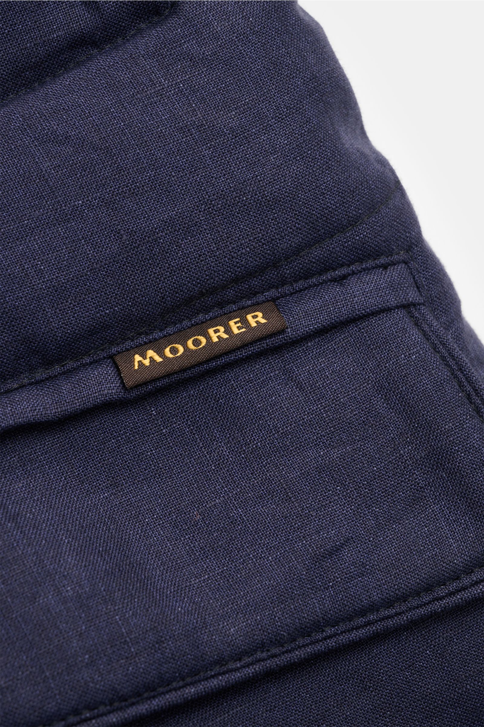 Close-up from above of the navy mottled linen fabric and stitching detail on the Moorer Down jacket 'Zavyer' navy mottled, featuring a brown label with gold MOORER lettering. The elegant quilted jacket 'Zavyer' by MOORER will see you through the transitio