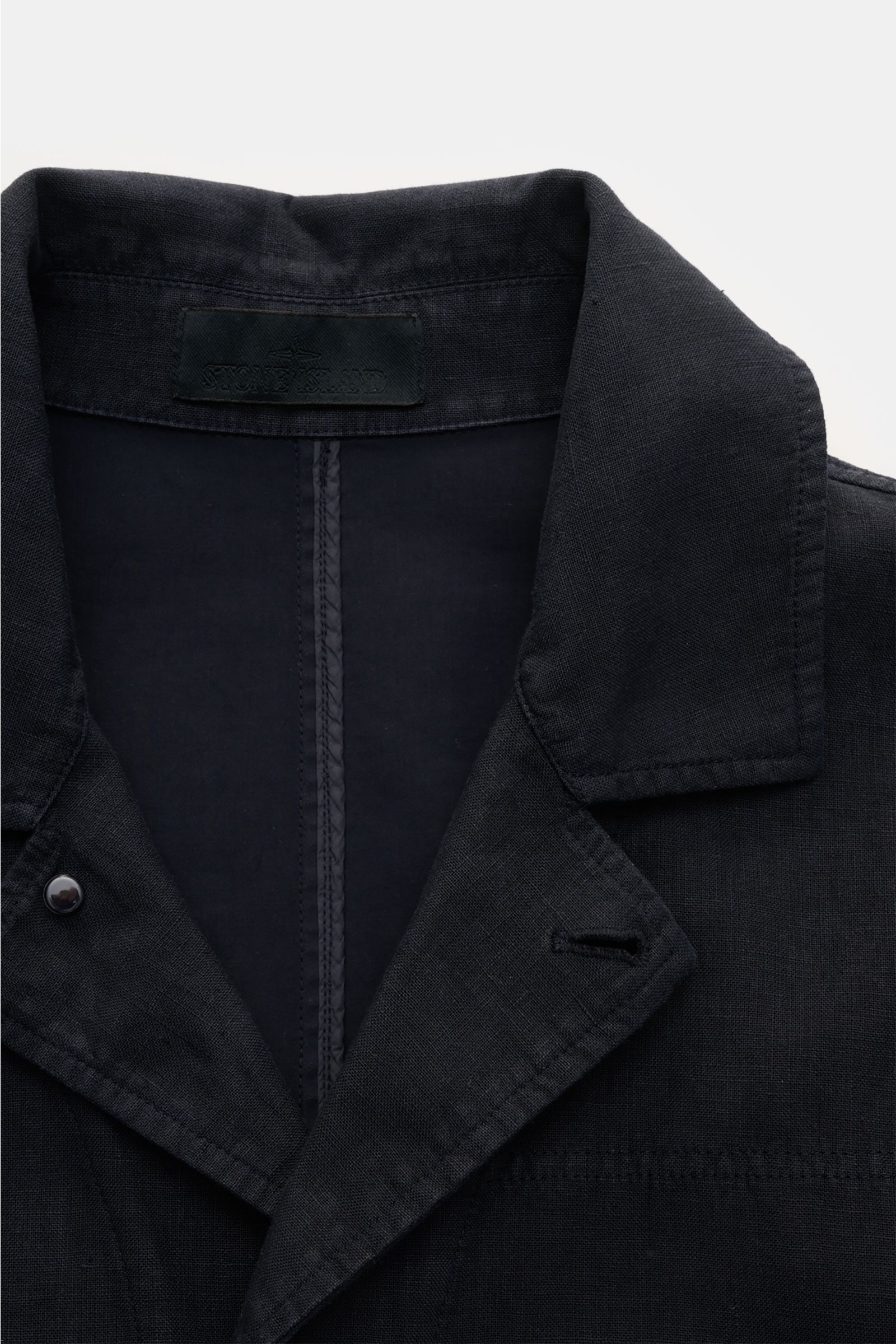 Close-up front view of the Stone Island Jacket 'Ghost Piece' navy, showcasing its linen and microfibre blend fabric, slim fit, concealed button placket, adjustable collar, hip pockets with flap, tonal sleeve badge, and snap button cuffs. Springtime meets 