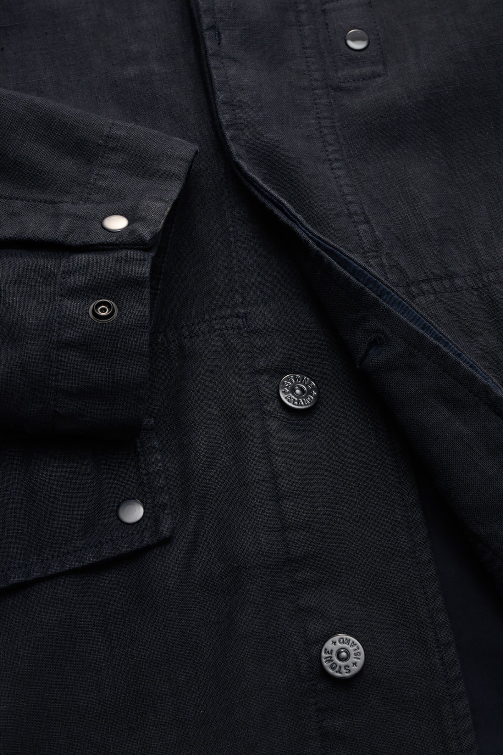 Close-up front view of Stone Island Jacket 'Ghost Piece' navy in linen and microfiber blend, showing concealed button placket, snap cuffs, and tonal badge. Springtime meets casual: This STONE ISLAND jacket from the 'Ghost' Capsule has been made from a lin