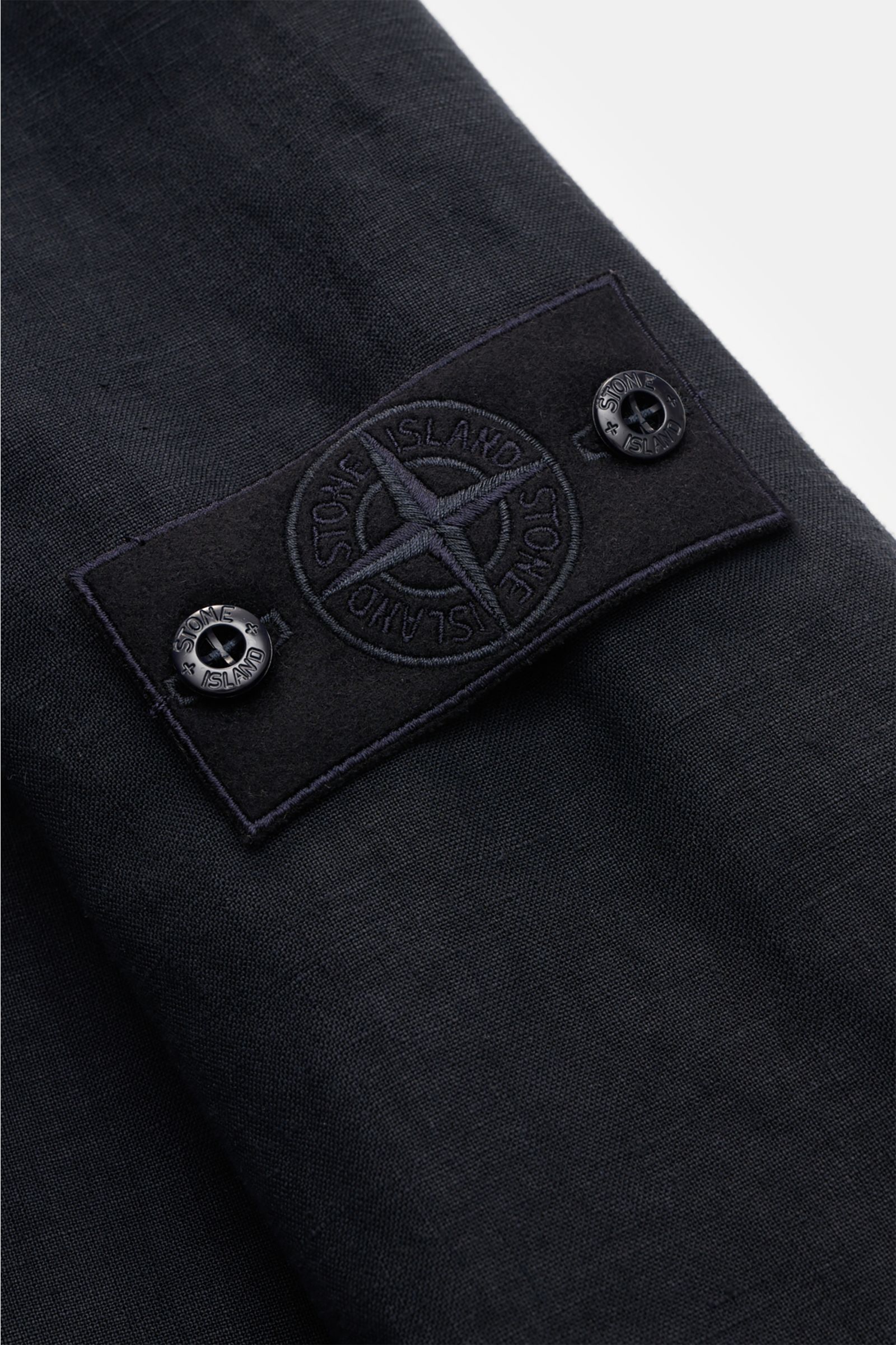 Close-up of the sleeve of the Stone Island Jacket 'Ghost Piece' navy showing the tonal badge with buttons, photographed from above.