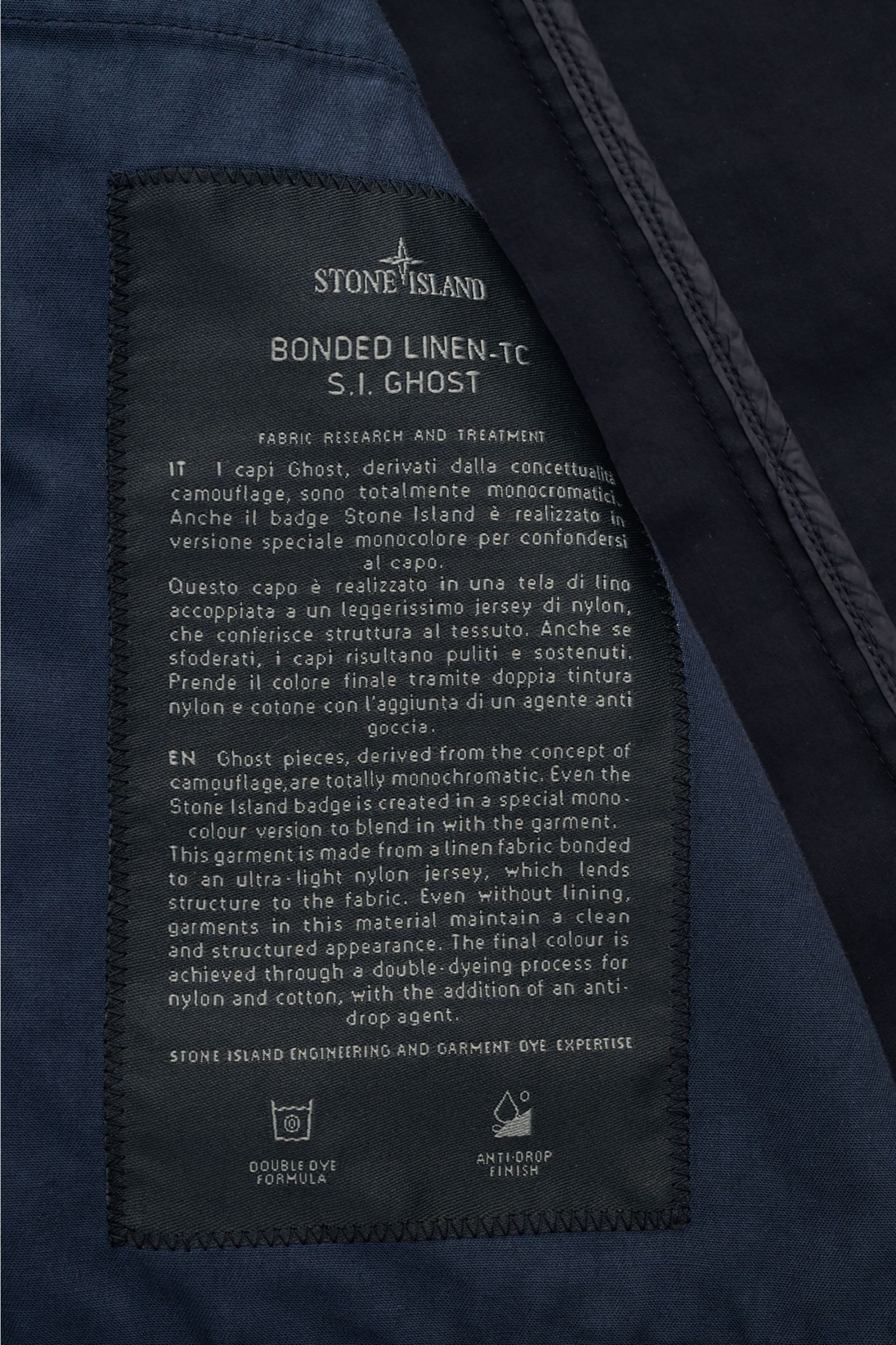 Close-up inside view of the Stone Island Jacket 'Ghost Piece' navy showing the black fabric label with detailed fabric research and treatment text. Springtime meets casual: This STONE ISLAND jacket from the 'Ghost' Capsule has been made from a linen blend