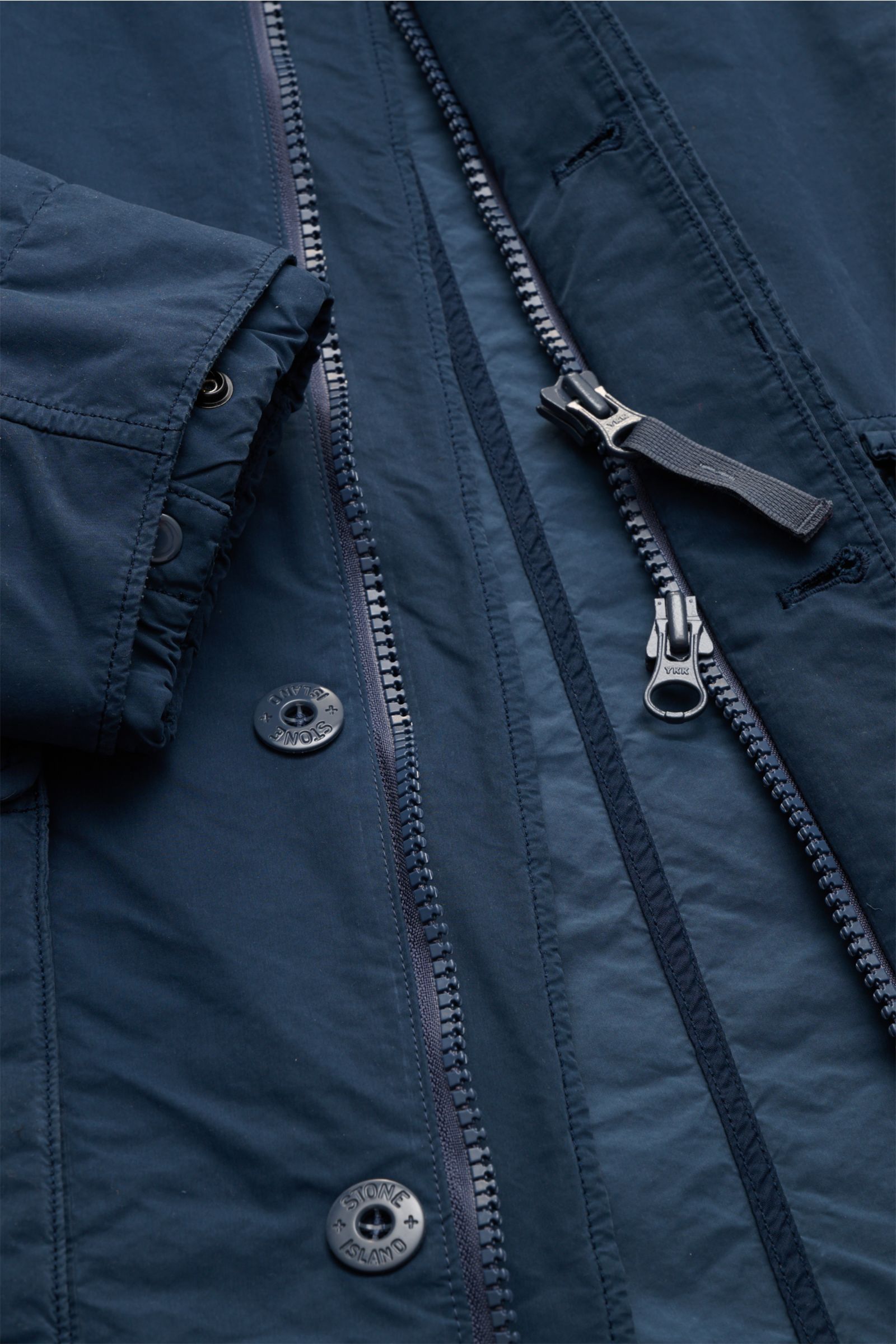 Stone Island Jacke 'Ghost Piece' dunkelblau, Detailaufnahme von Reißverschluss, Knöpfen, Kapuze, elastischem Ärmelbündchen aus hochwertiger Microfaser.