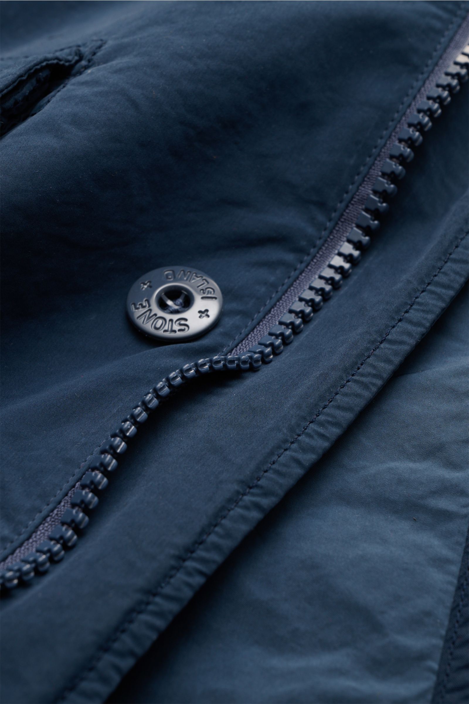 Nahaufnahme der Stone Island Jacke 'Ghost Piece' dunkelblau aus der Ghost Capsule Collection, Fokus auf Reißverschluss und Logo-Knopf.