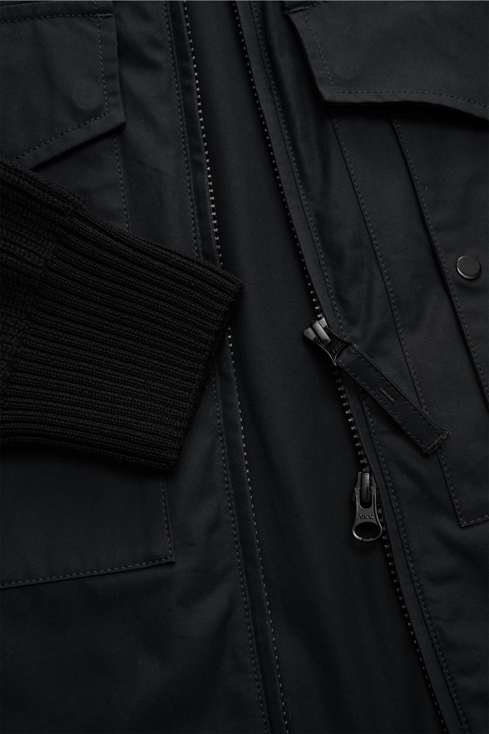 Close-up front view of Stone Island Blouson 'Ghost Piece' schwarz, showing black cotton corpus, wool knit sleeve cuff, two-way zipper, flap pockets, tonal badge, slim fit, soft texture, high collar, and flexible ribbed cuffs. Cooles, monochromes Essential