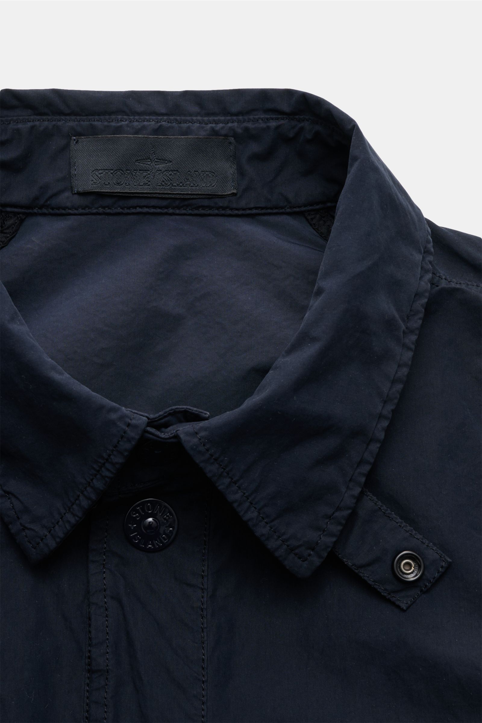 Close-up front view of the collar and upper front of the Stone Island Jacke 'Ghost Piece' navy, featuring a garment dyed look, high-quality microfiber, soft touch, slim fit, snap button placket, turn-down collar with button tab, tonal compass badge on the