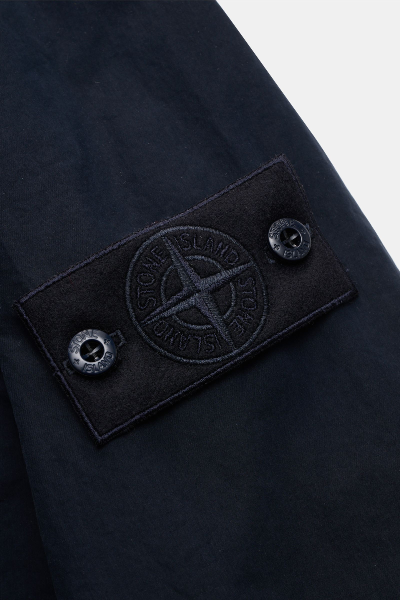 Close-up of the tonal compass badge on the sleeve of the Stone Island Jacke 'Ghost Piece' navy, showing fine stitching and button details, photographed from a side angle.

Additional description (not in alt tag, for reference):
Urbanes Essential: Die STON