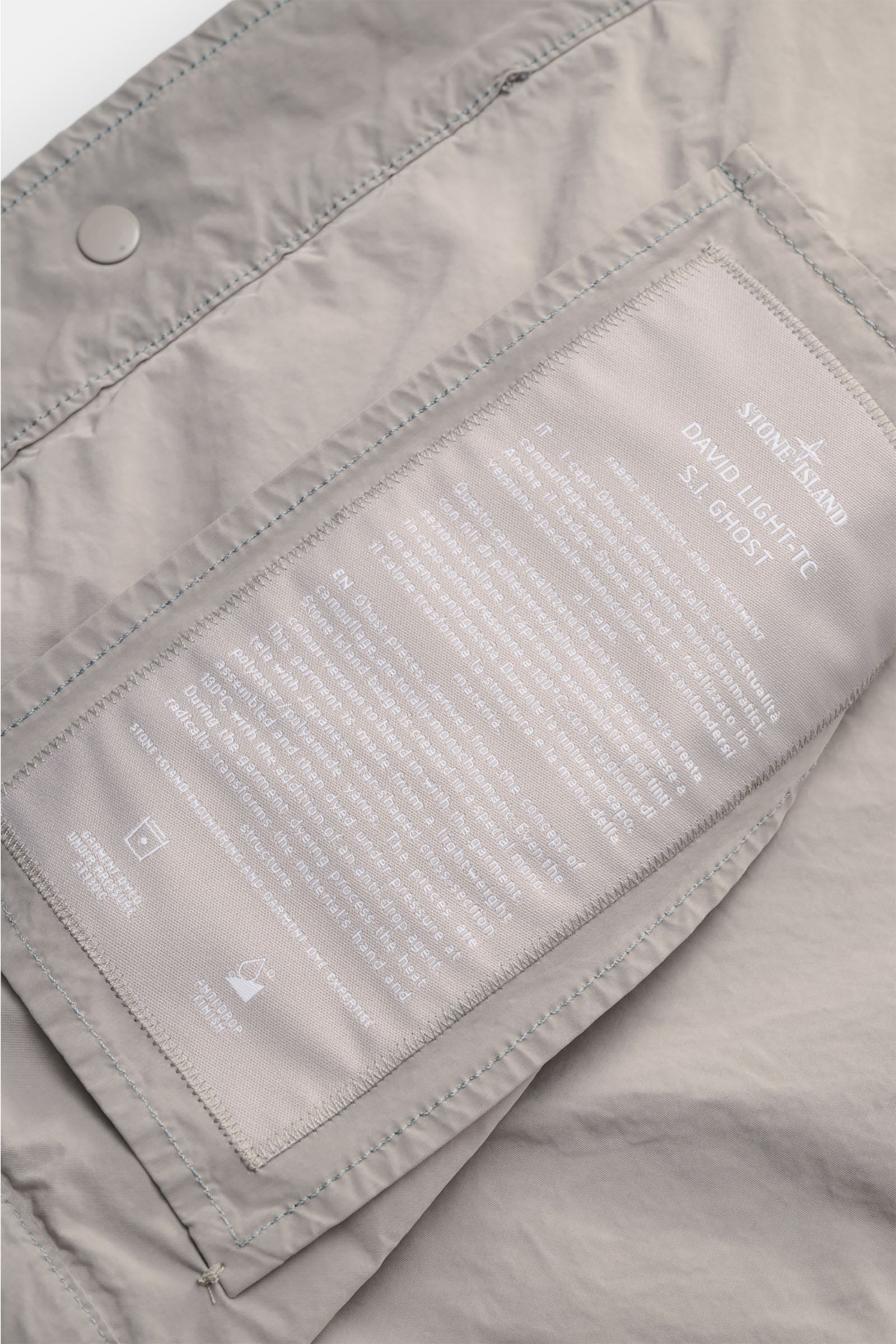 Close-up inside view of Stone Island Jacket 'Ghost Piece' light grey showing fabric label, snap button placket, and high-quality microfibre details. Urban essential: This STONE ISLAND jacket from the 'Ghost Collection' impresses with its casual design and