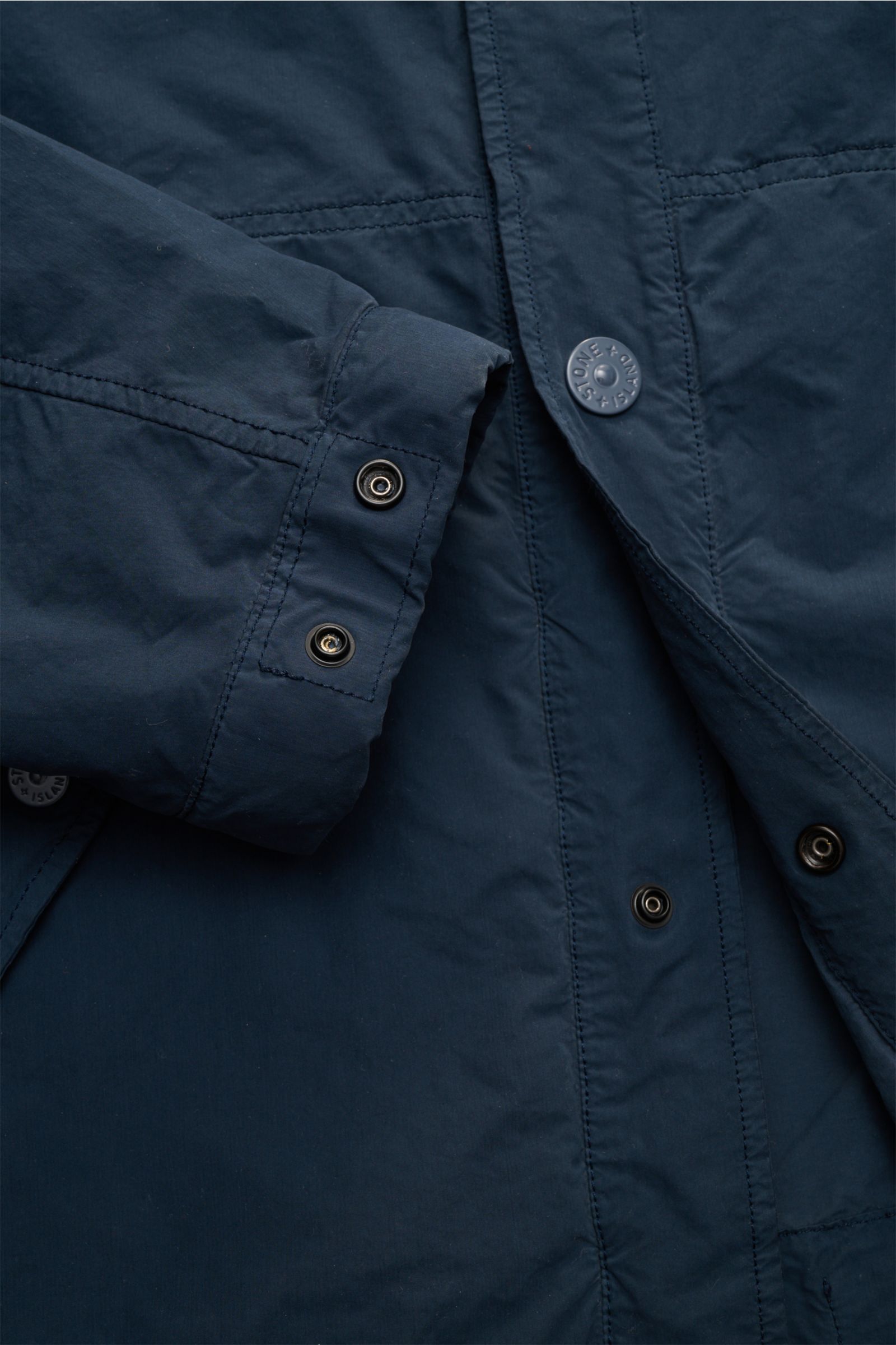 Nahaufnahme der Stone Island Jacke 'Ghost Piece' dunkelblau aus der 'Ghost Collection', zeigt Druckknopfleiste, Ärmel mit Druckknopf und hochwertige Microfaser.