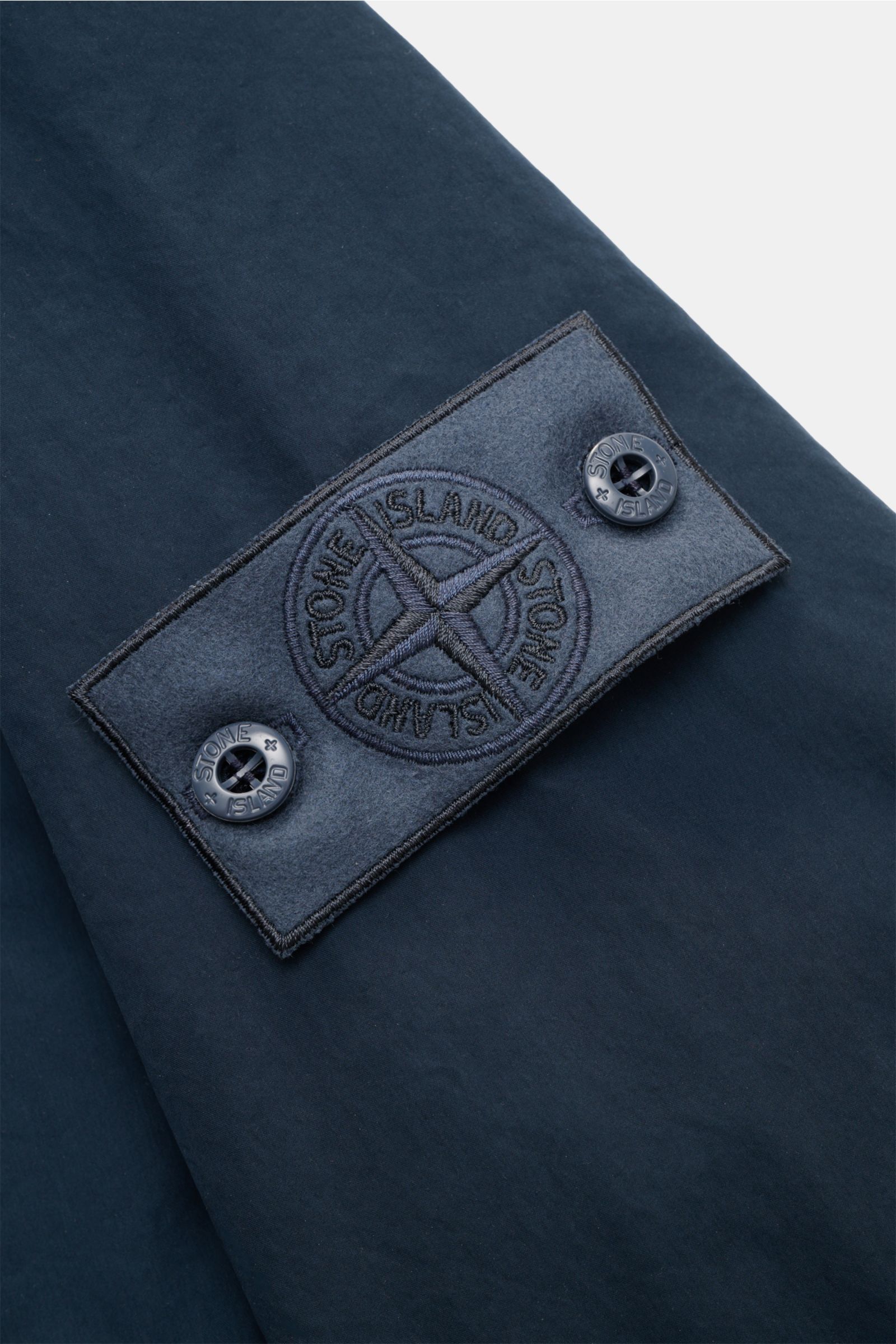 Nahaufnahme des tonalen Kompass-Badges auf dem Ärmel der dunkelblauen Stone Island Jacke 'Ghost Piece' aus hochwertiger Microfaser.