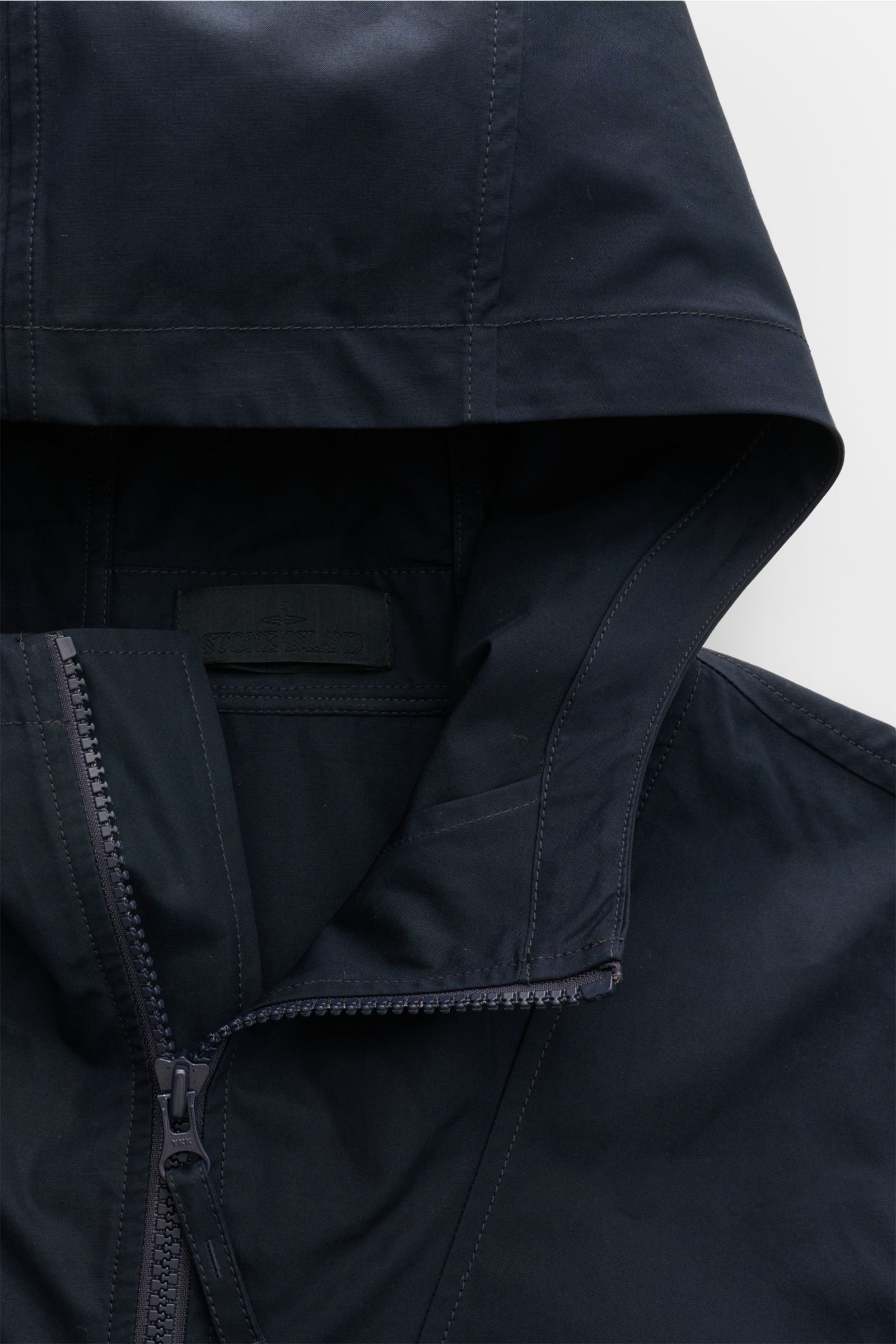 Close-up front view of the Stone Island Jacke 'All-Weather S.I. Ghost Piece' navy, showing the hood, robust two-way zipper, and smooth cotton canvas fabric. Funktion trifft Komfort: Die STONE ISLAND Jacke aus der 'Ghost' Capsule wurde aus einem Baumwollca