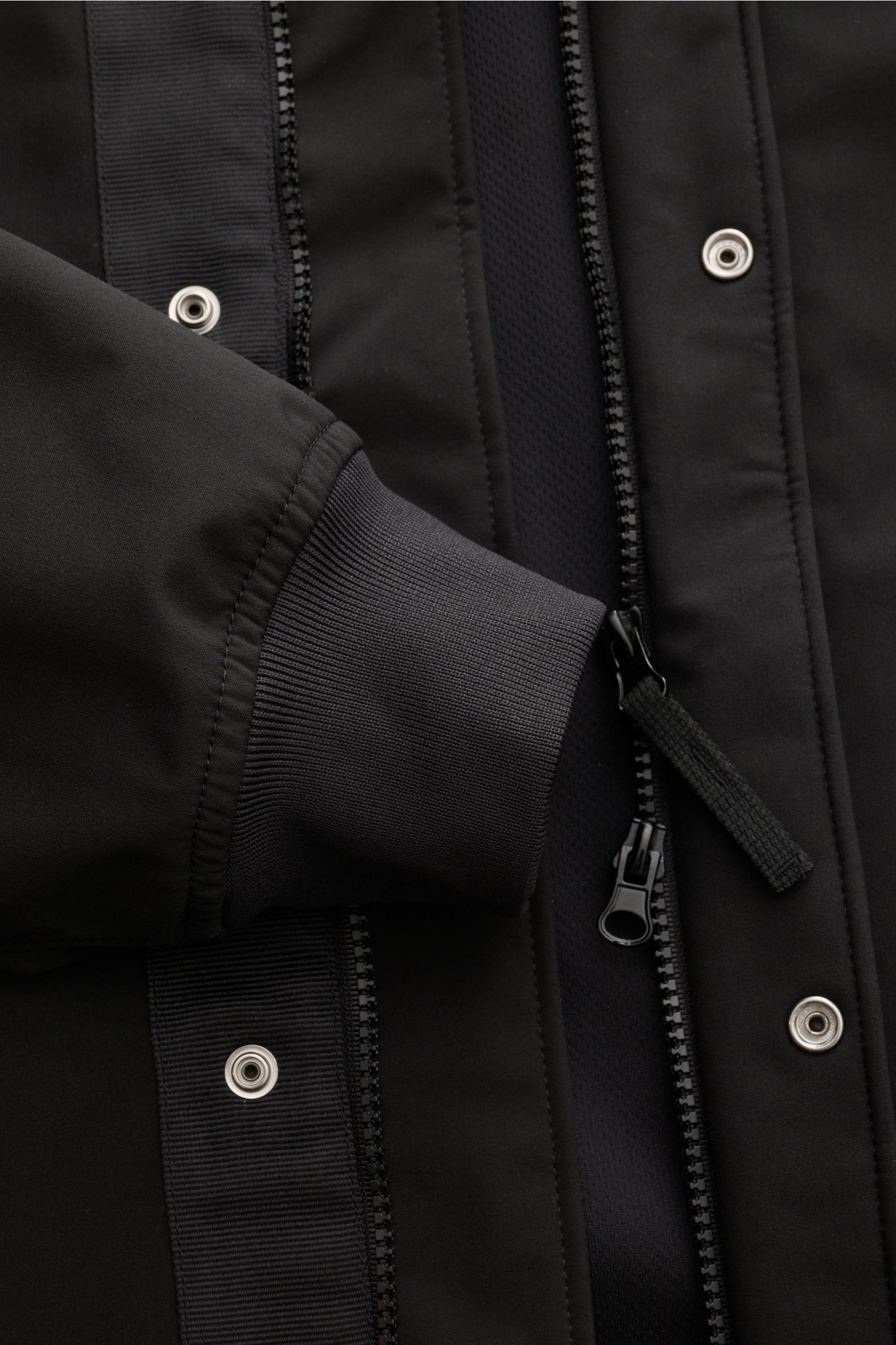Nahaufnahme des Stone Island Blouson 'Light Soft Shell-R' schwarz von vorne mit Fokus auf Reißverschluss, Druckknöpfen und elastischem Ärmelbündchen.