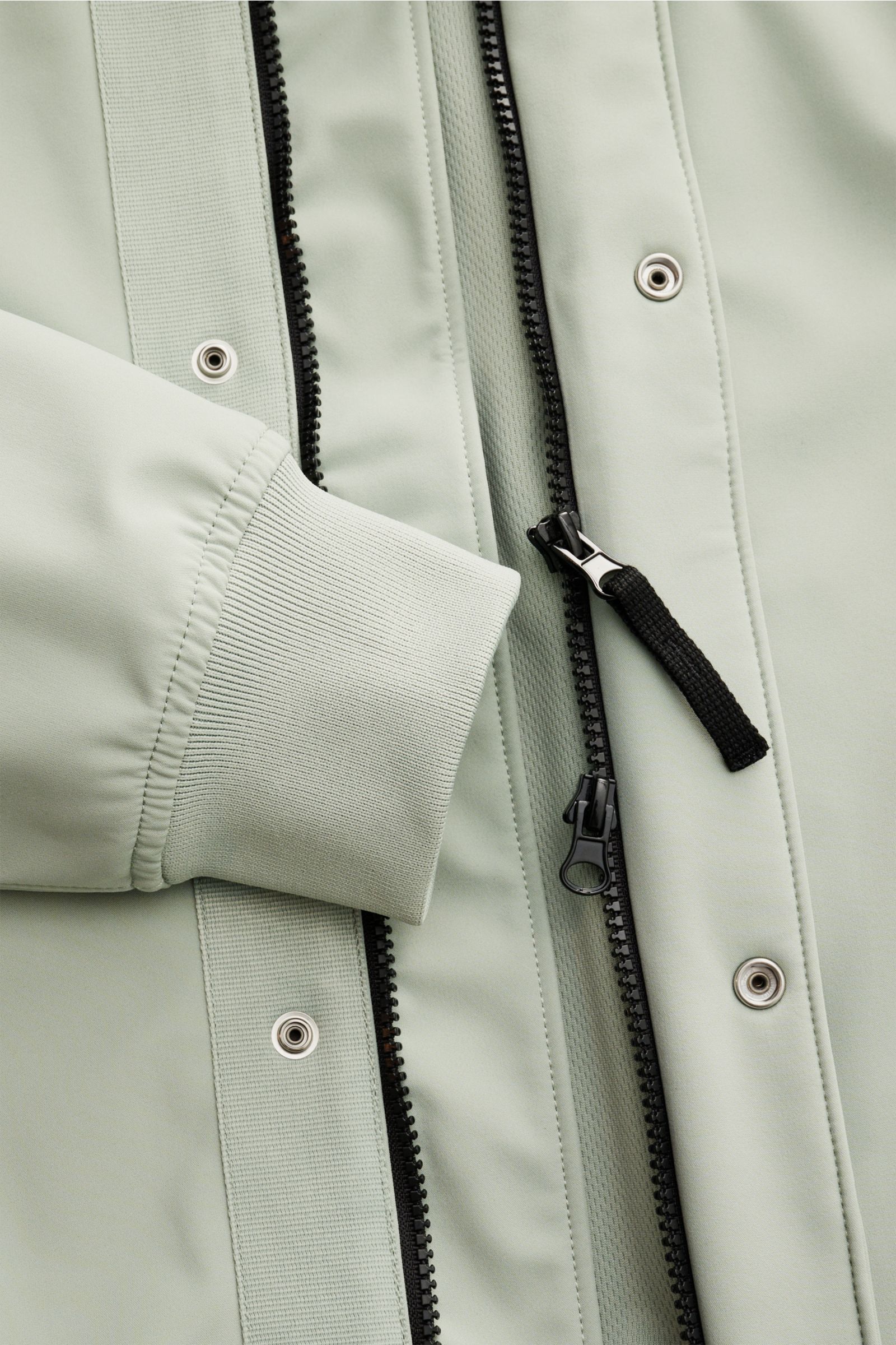 Nahaufnahme von Ärmelbündchen und zwei-Wege-Reißverschluss des Stone Island Blouson 'Light Soft Shell-R' salbei aus glattem, wind- und wasserabweisendem Microfaserstoff.