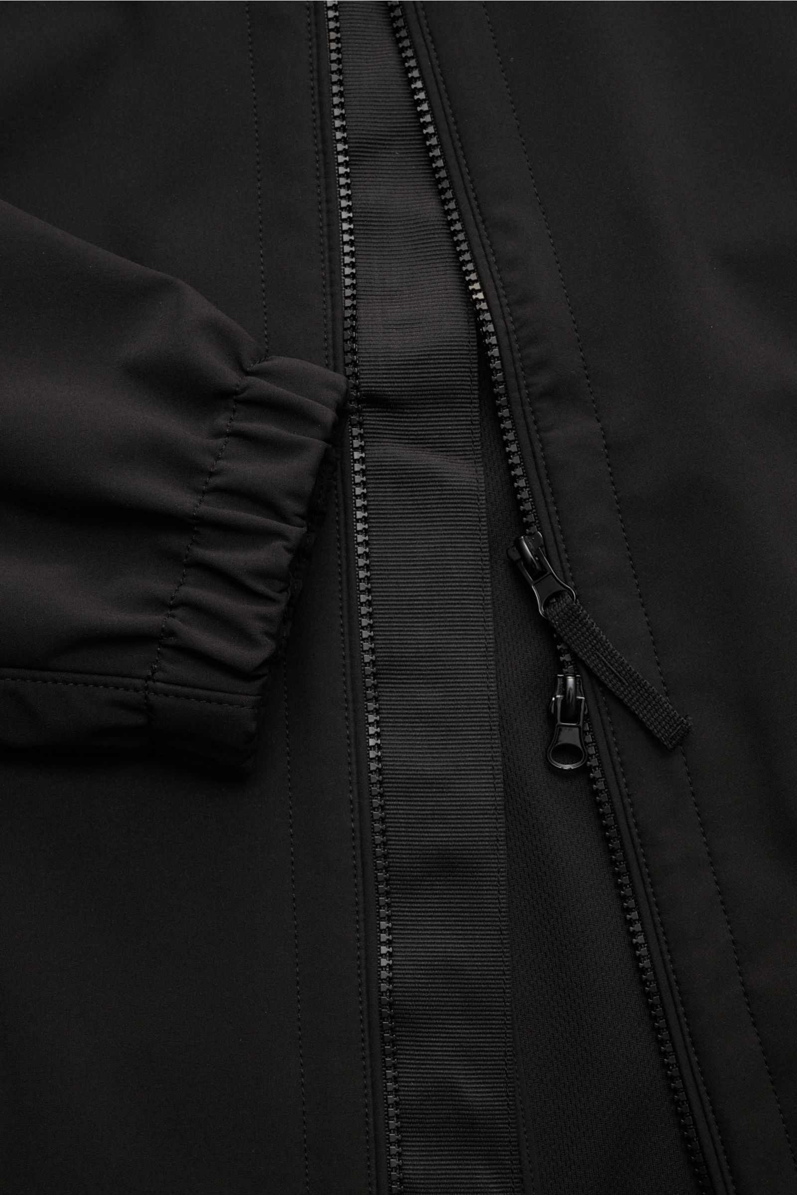 Close-up front view of the Stone Island Jacke 'Light Soft Shell-R' schwarz showing the two-way zipper, elastic sleeve cuff, and smooth black microfiber fabric. Stil trifft Funktion: Die Soft Shell Jacke von STONE ISLAND überzeugt mit sportivem Design sowi