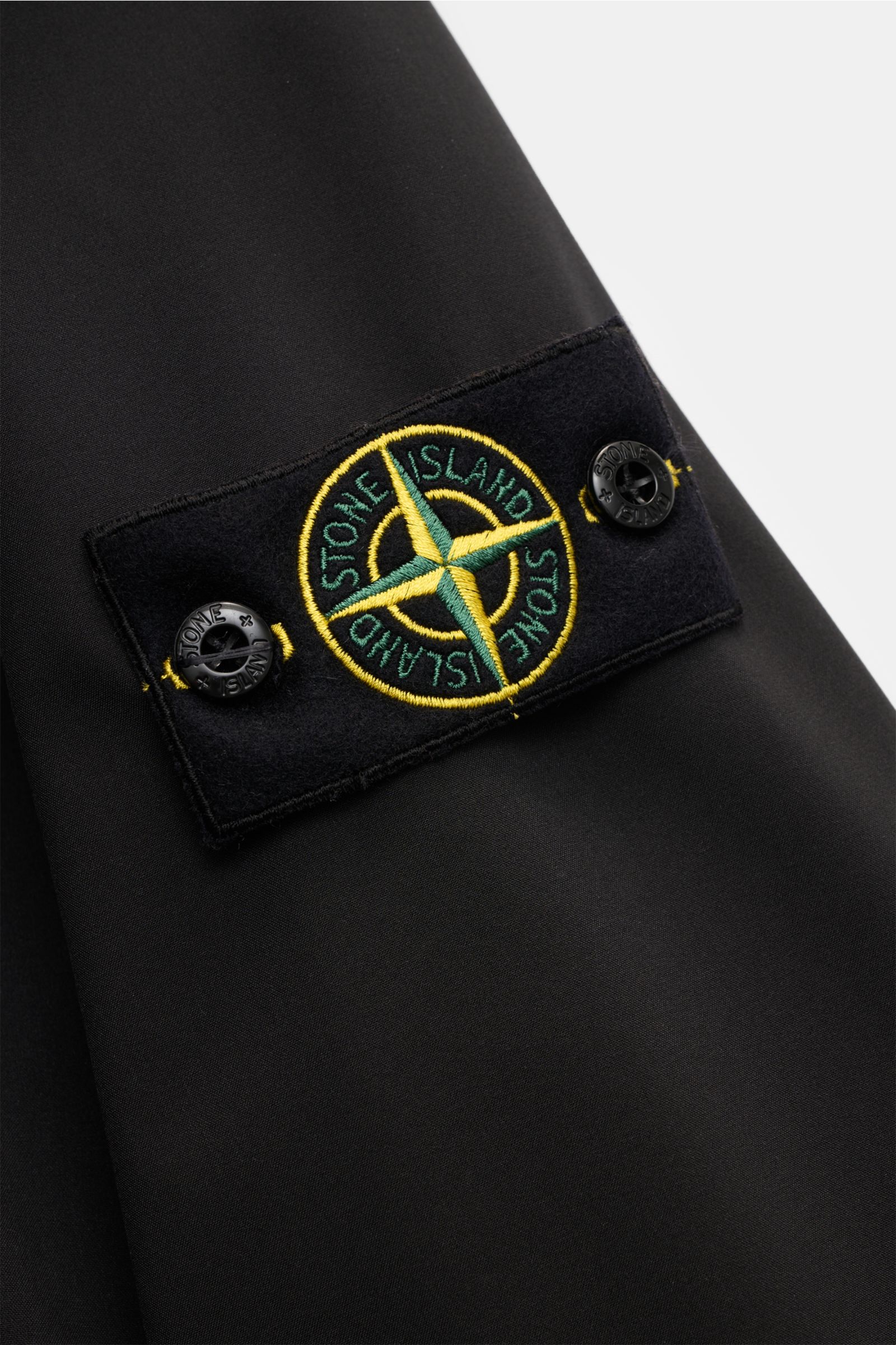 Stone Island Jacke 'Light Soft Shell-R' schwarz, Nahaufnahme des Kompass-Badges auf dem Ärmel, glatte Microfaser, wind- und wasserabweisend.