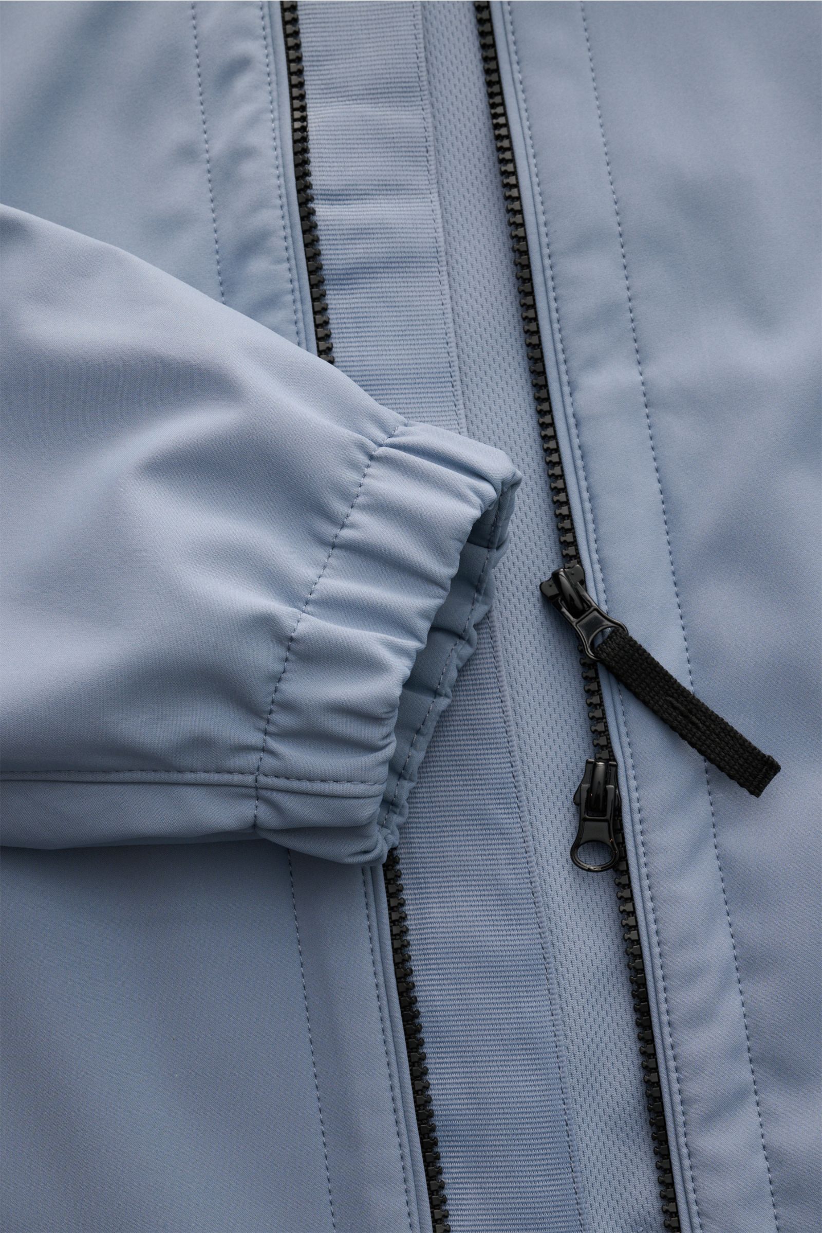 Nahaufnahme der Stone Island Jacke 'Light Soft Shell-R' rauchblau von vorne, zeigt elastisches Ärmelbündchen, zwei-Wege-Reißverschluss und glattes Microfasermaterial, wind- und wasserabweisend mit geschmeidigem Futterstoff.