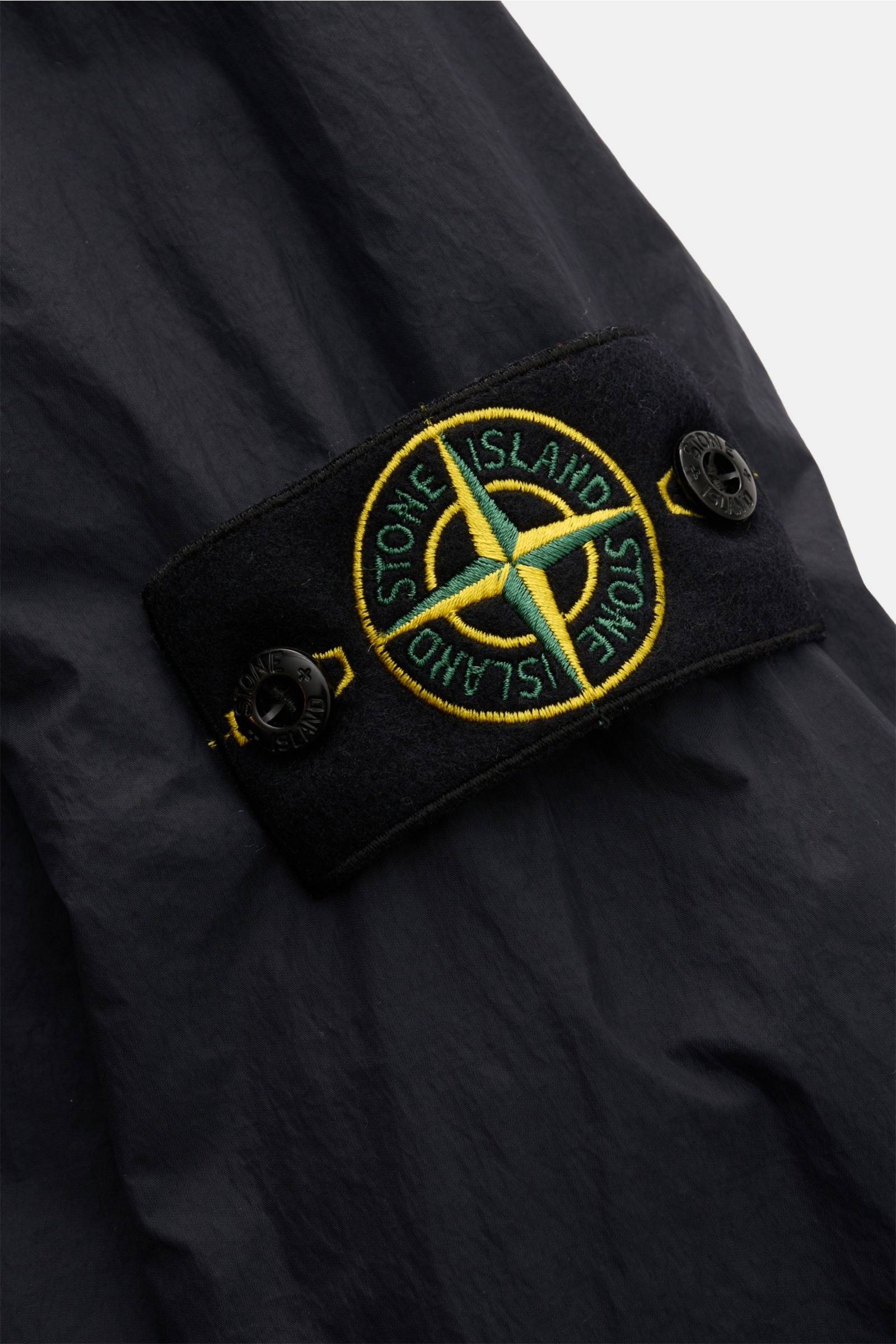 Nahaufnahme des Stone Island Blouson 'Garment Dyed Crinkle Reps NY' navy Ärmels mit Kompass-Badge auf hochwertigem, wind- und wasserabweisendem Microfaser-Material.