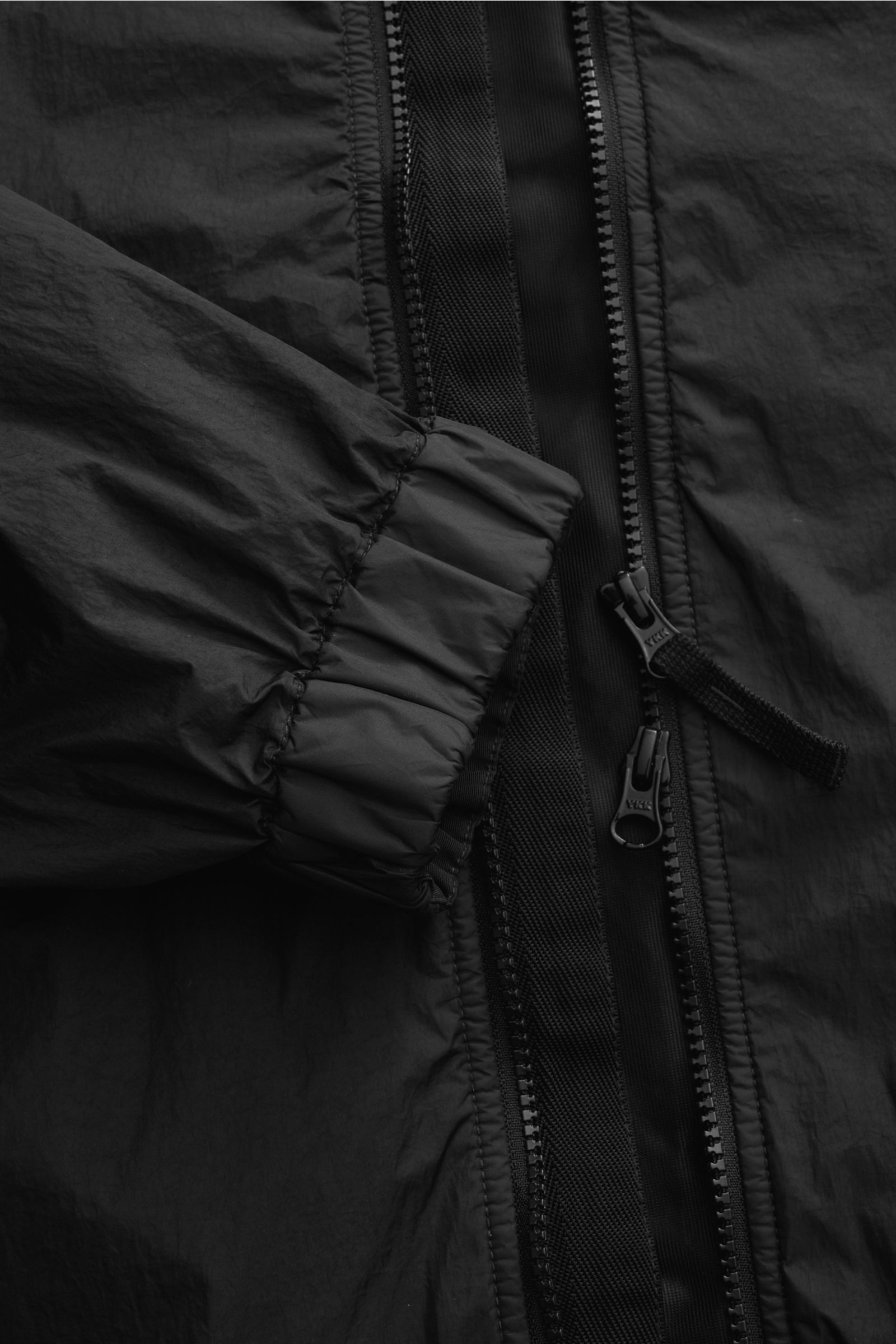 Nahaufnahme des Stone Island Blouson 'Garment Dyed Crinkle Reps NY' schwarz, Fokus auf Reißverschluss und elastischem Ärmelbündchen, leichte Microfaser mit Knittereffekt, wind- und wasserabweisend.