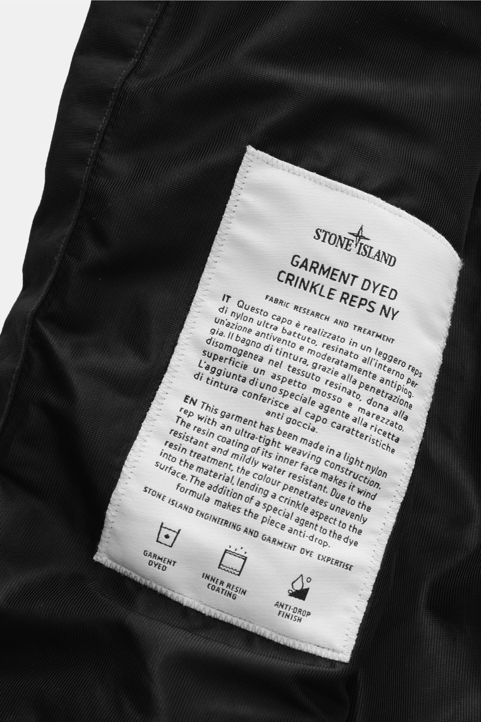 Nahaufnahme des weißen Textlabels im Inneren des Stone Island Blouson 'Garment Dyed Crinkle Reps NY' schwarz, das Material- und Pflegehinweise zeigt.