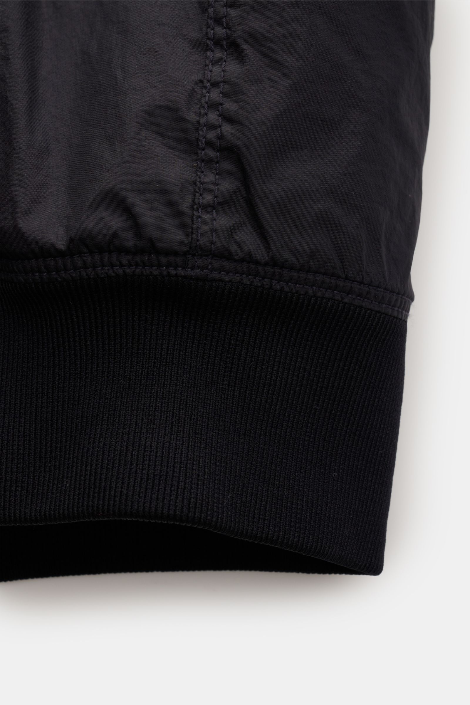 Close-up side view of the cuff of the Stone Island Jacke 'Garment Dyed Crinkle Reps NY' dark navy, showing finely stitched lightweight microfiber fabric with a resin coating that creates a crinkled effect, and a ribbed elastic hem cuff. Funktion trifft St