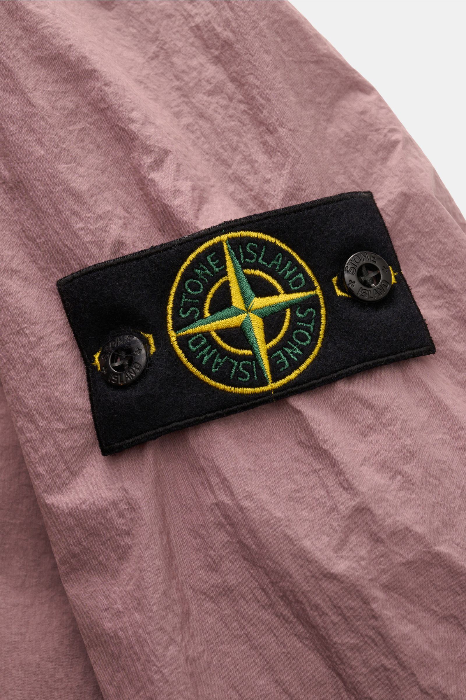 Nahaufnahme der Stone Island Jacke 'Garment Dyed Crincle Reps NY' altrosa, Fokus auf Kompass-Badge am Ärmel, technische Microfaser, wasserabweisend, windblockend.