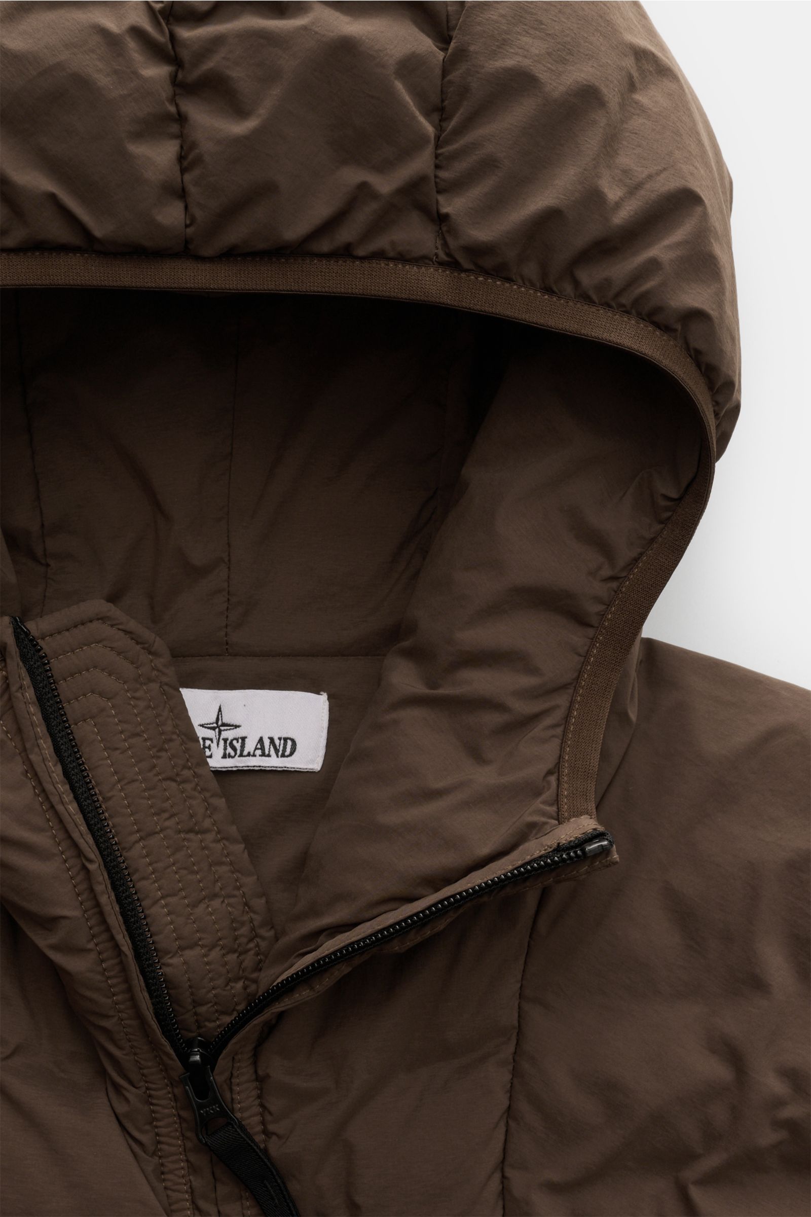 Nahaufnahme der braunen Stone Island Daunenjacke 'Seamless Tunnel Nylon Down-TC' von oben, zeigt Kapuze, wasserabweisendes Material und Reißverschluss.