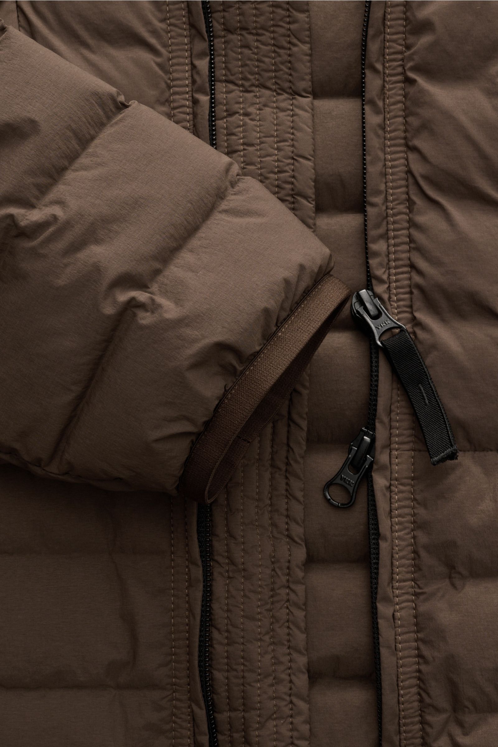 Nahaufnahme der Stone Island Daunenjacke 'Seamless Tunnel Nylon Down-TC' braun, zeigt Reißverschluss, elastischen Ärmelabschluss und Microfaserstoff.