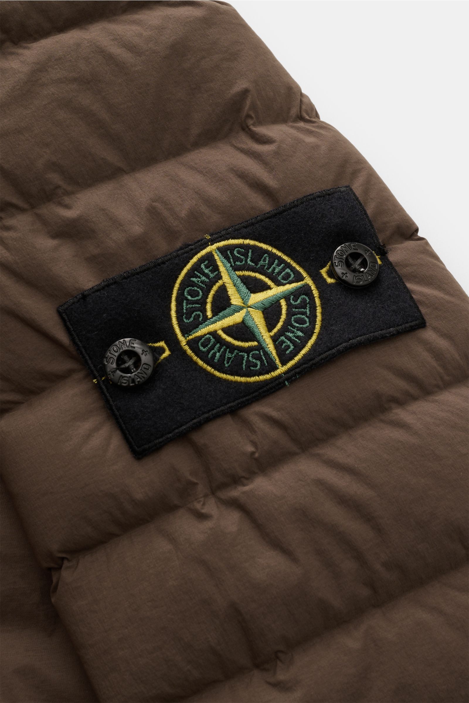 Stone Island Daunenjacke 'Seamless Tunnel Nylon Down-TC' braun, Detailansicht des Kompass-Badges auf wasserabweisendem, leicht elastischem Material.