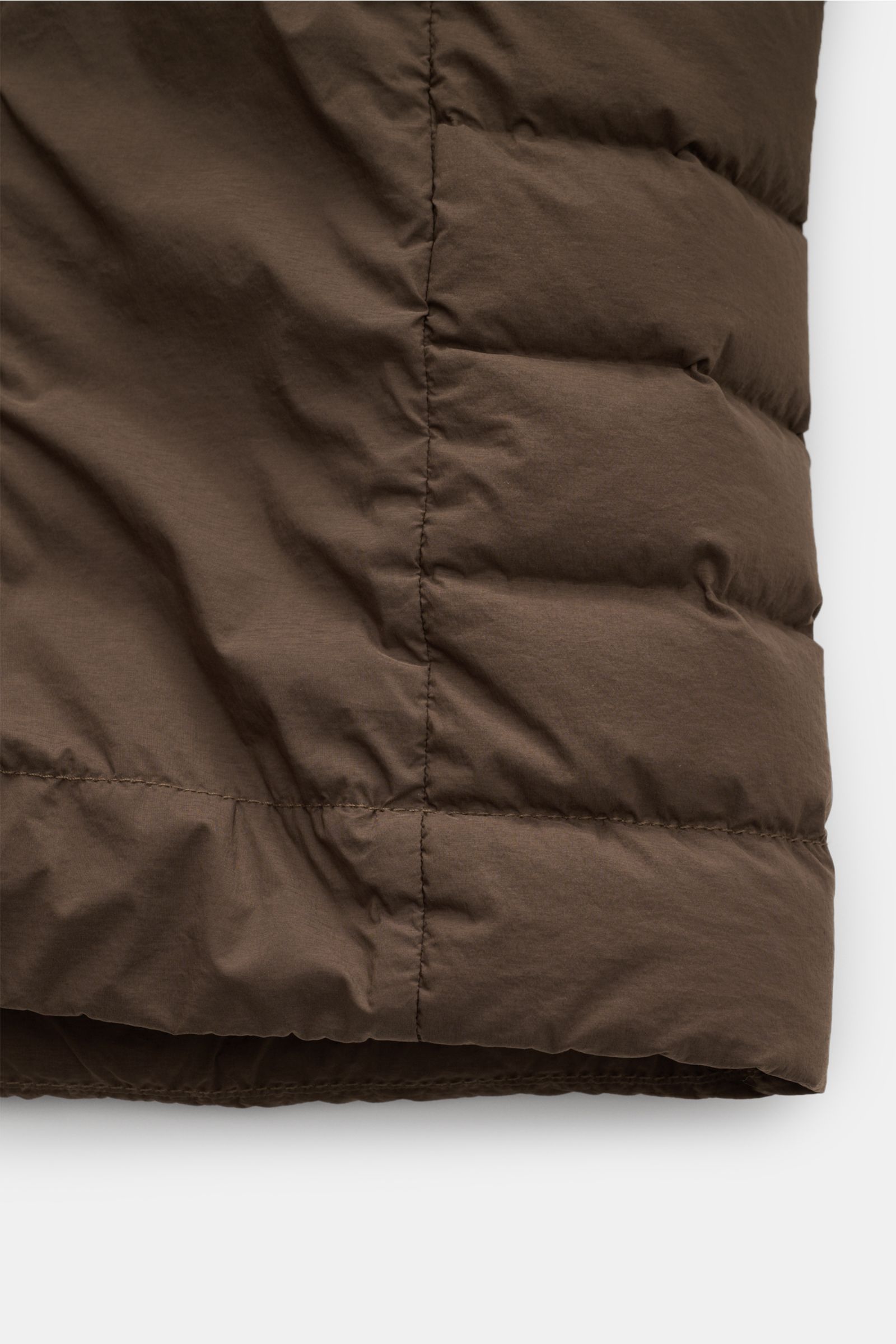Nahaufnahme der braunen Stone Island Daunenjacke 'Seamless Tunnel Nylon Down-TC' mit leichter Daunenfüllung und glattem, wasserabweisendem Microfaserstoff, Detailansicht vom Saum.
