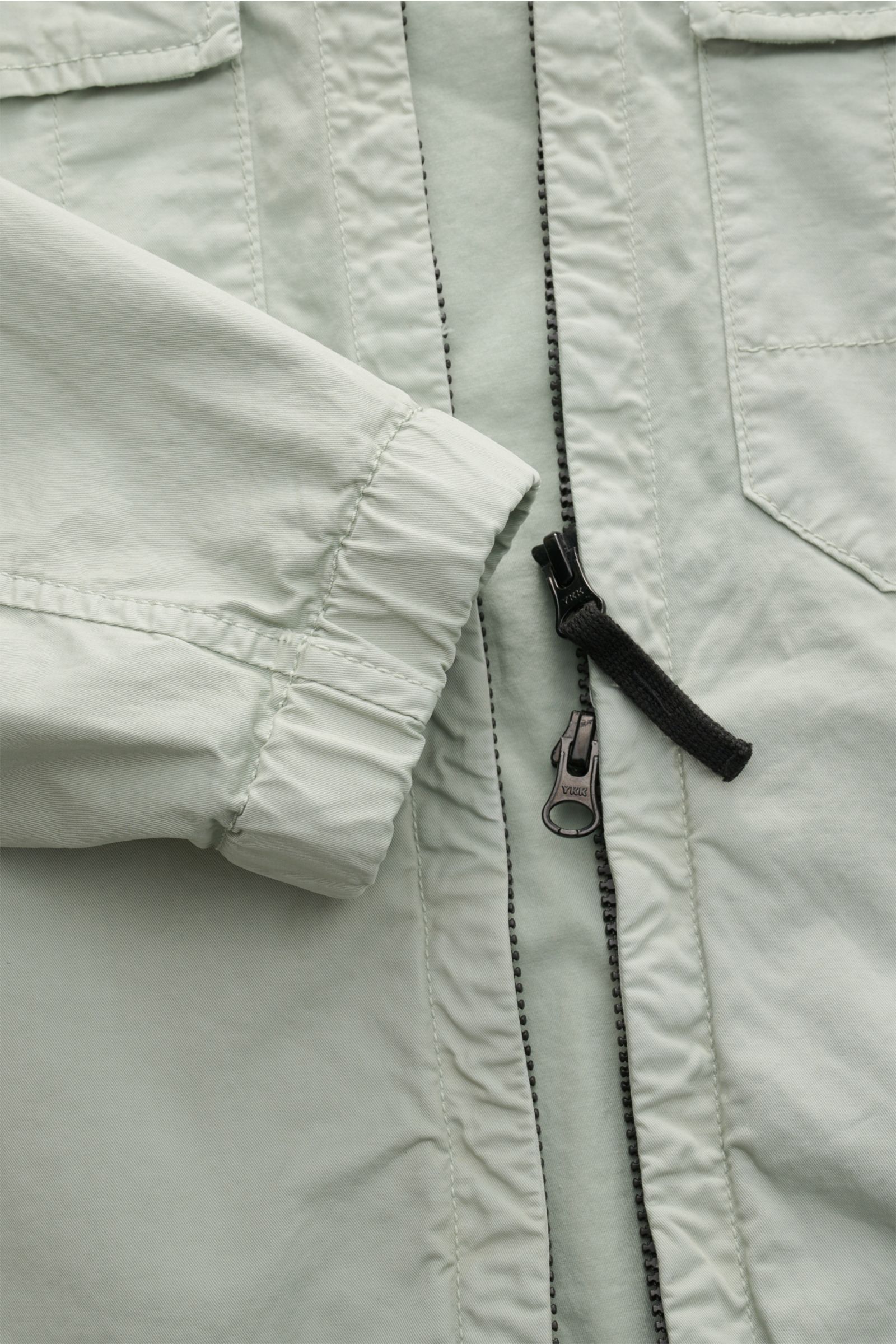 Stone Island Blouson 'Stretch Cotton Twill-TC' salbei, Detailaufnahme von elastischem Ärmelbündchen, robustem Zwei-Wege-Reißverschluss und Brusttasche.