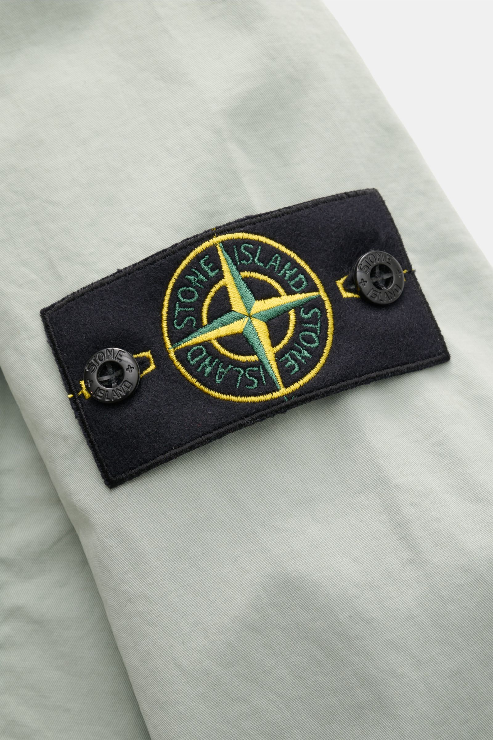Nahaufnahme des Stone Island Blouson 'Stretch Cotton Twill-TC' salbei mit elastischer Baumwolle und gesticktem Logo auf dem Ärmel.