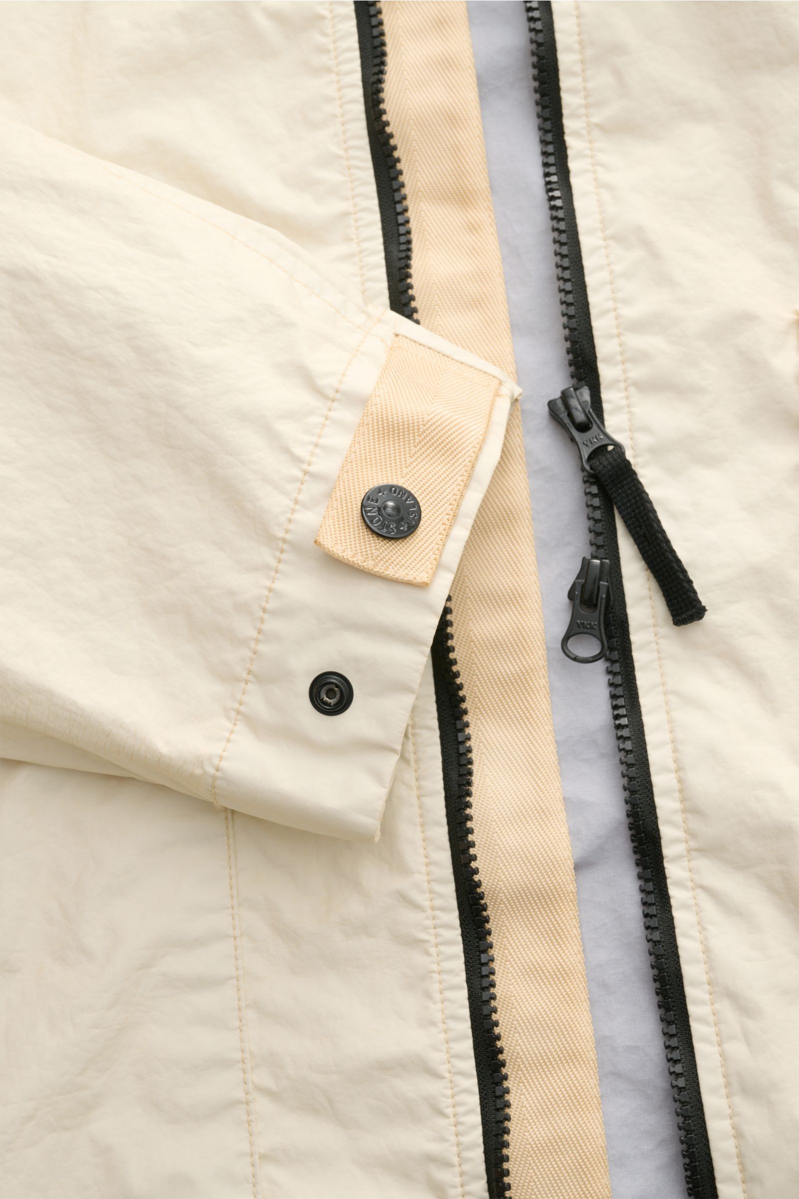 Stone Island Jacke 'Membrana' creme, Nahaufnahme von Ärmel mit Knopfleiste und teilweisem Zwei-Wege-Reißverschluss, wind- und wasserabweisend.