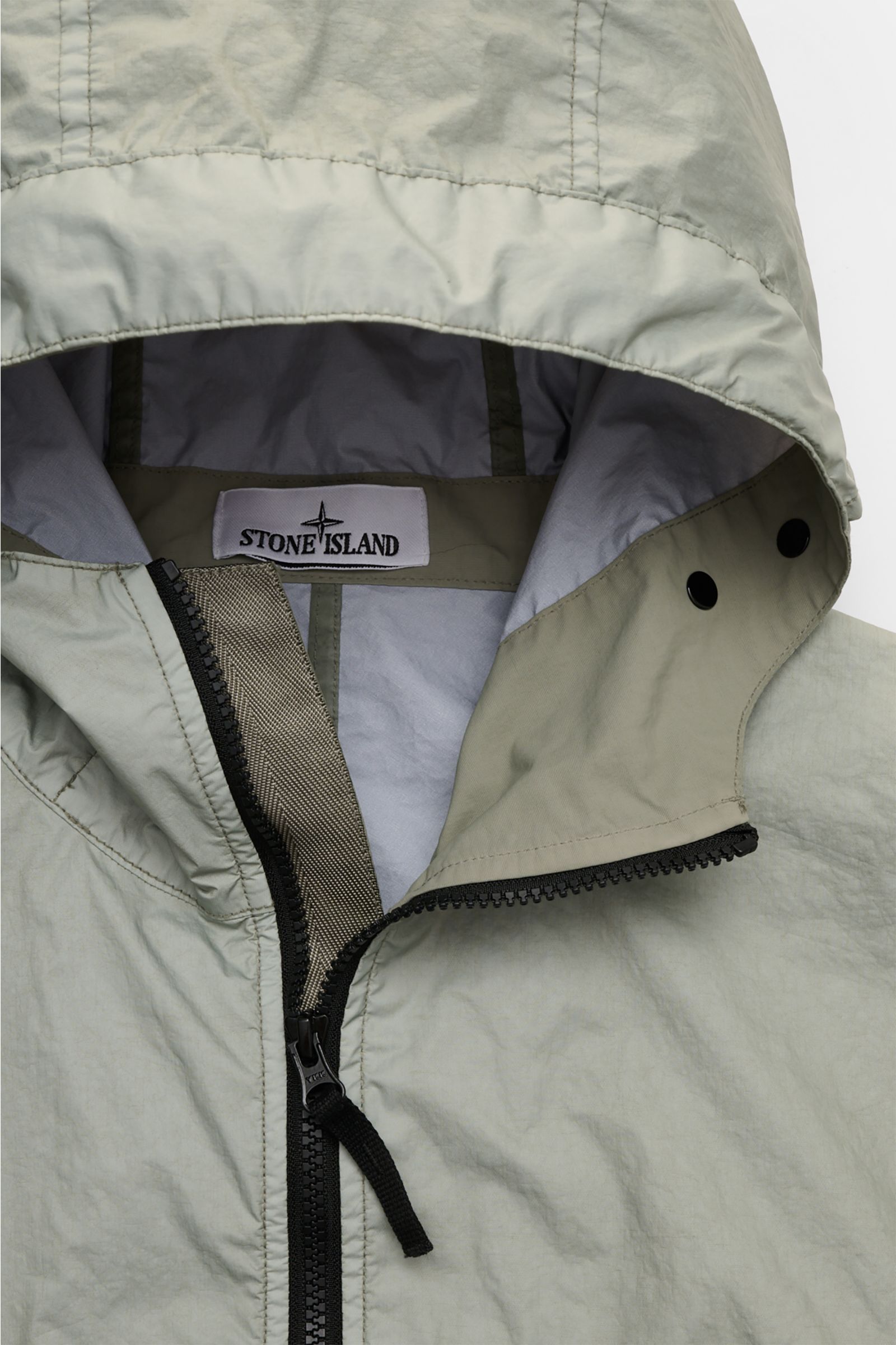 Close-up front view of Stone Island Jacket 'Membrana' sage featuring a hood, black two-way zipper, and visible brand label inside. Function meets style: The triple-layer functional fabric of this STONE ISLAND jacket is laminated with a breathable, water r