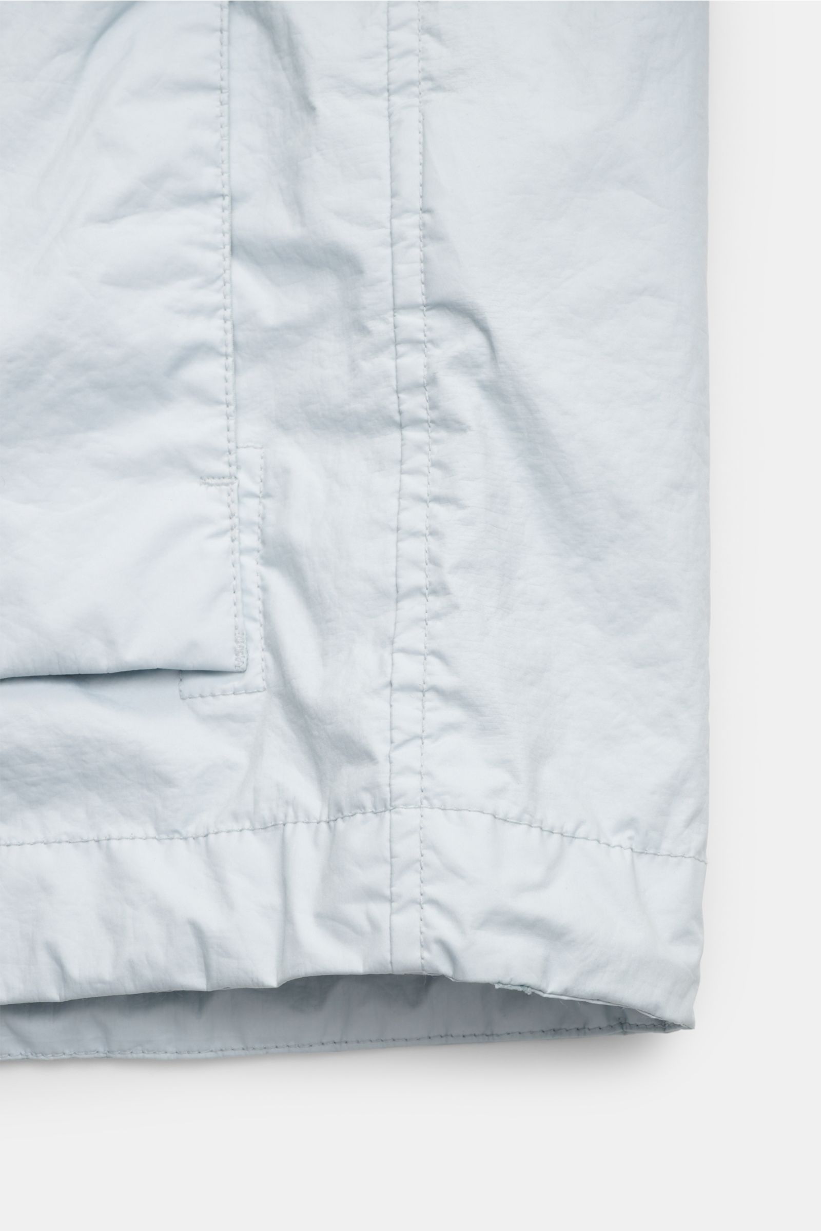 Close-up view of the lower front section of the Stone Island Jacke 'Membrana' hellgrau, showcasing the light gray microfiber fabric, visible stitching, and part of the front pocket flap. Funktion trifft Style: Das dreilagige, leichte Funktionsgewebe der S