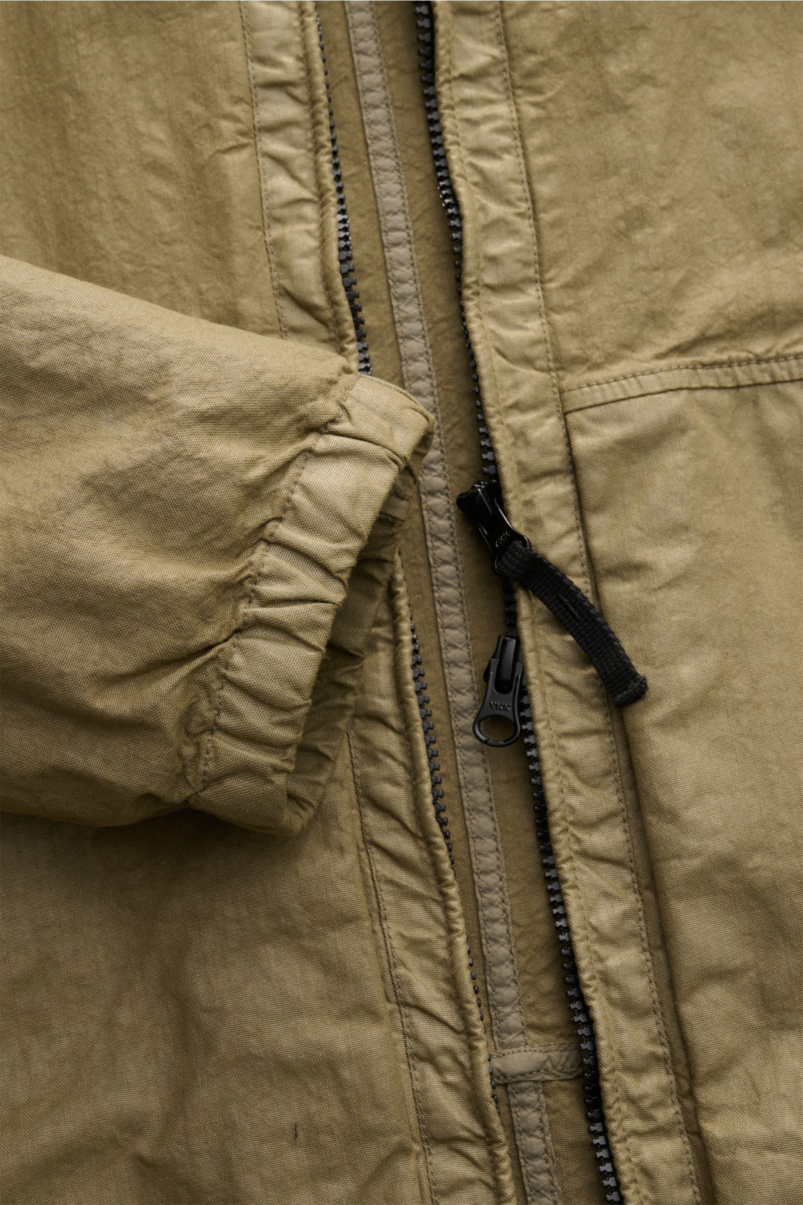 Nahaufnahme der Stone Island Jacke 'Organic-Look Nylon Panama-TC' oliv im Slim Fit, zeigt elastisches Ärmelbündchen und robusten Zwei-Wege-Reißverschluss aus dicht gewebtem, wasserabweisendem Microfaser-Canvas.