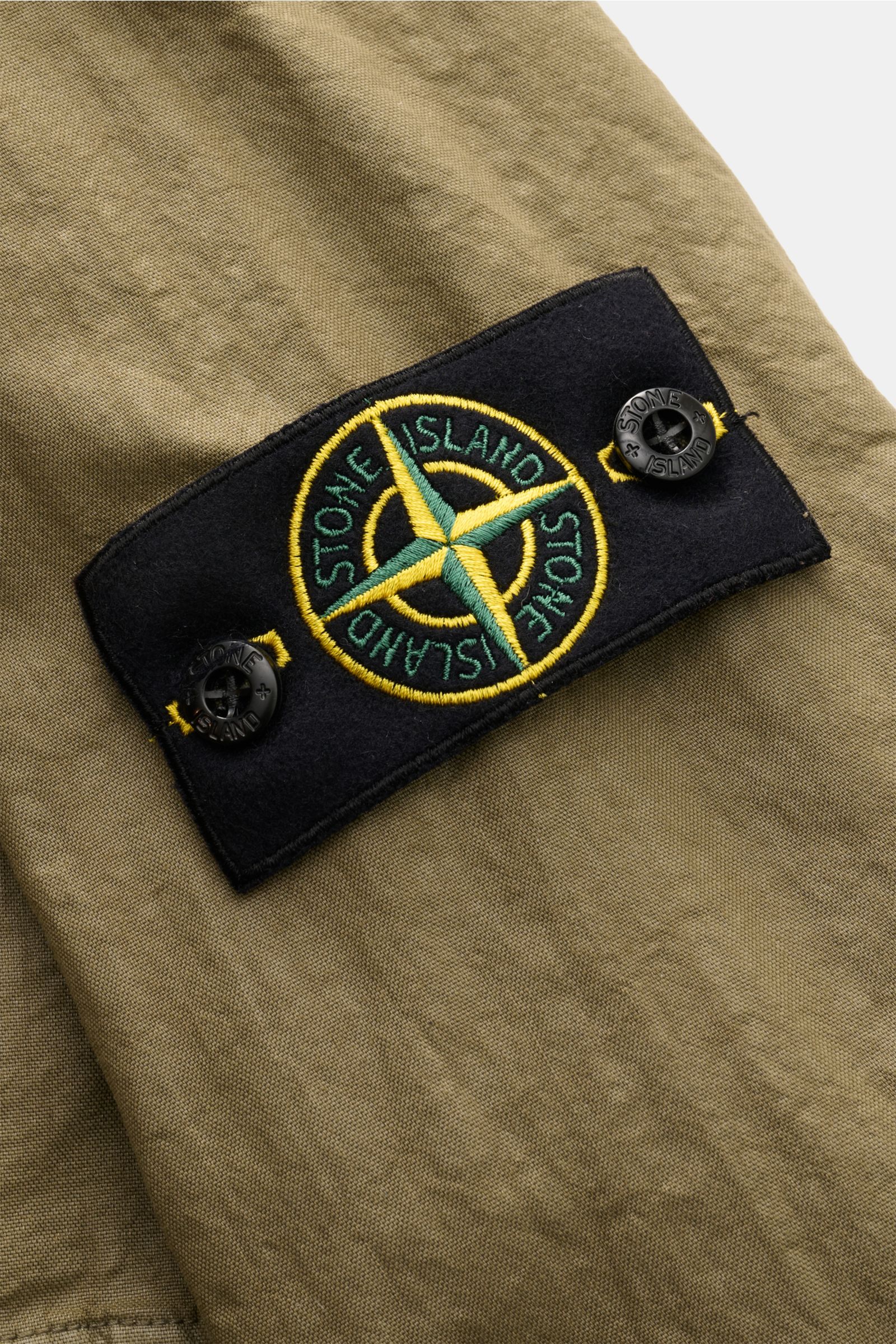 Nahaufnahme des Kompass-Badges auf dem Ärmel der Stone Island Jacke 'Organic-Look Nylon Panama-TC' oliv aus dicht gewebtem, wasserabweisendem Microfaser-Canvas.