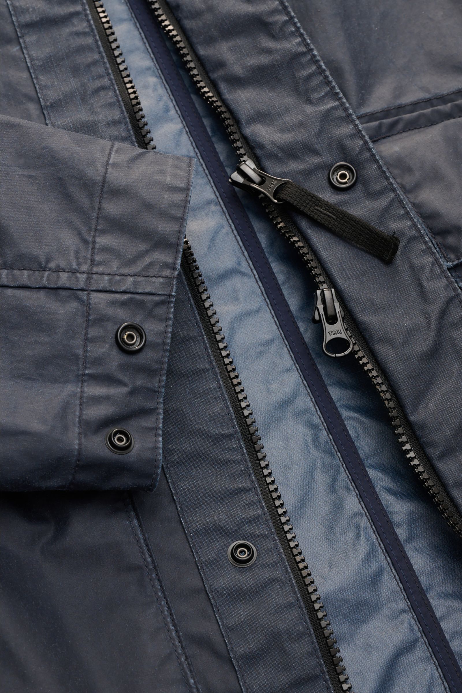 Close-up front view of Stone Island Waxed jacket 'Waxed Pigment Cotton Tela' navy showing the water-repellent waxed cotton-polyester fabric, robust two-way YKK zipper with black pull tab, snap button storm flap, and adjustable cuff with snap buttons. 

