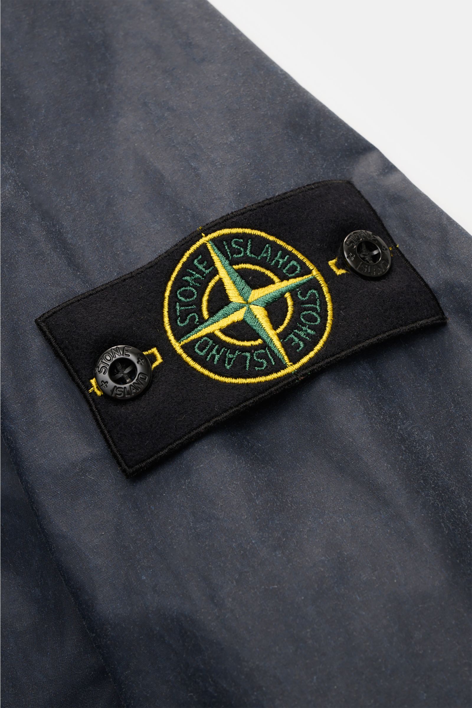 Stone Island Waxed jacket 'Waxed Pigment Cotton Tela' navy close-up of signature compass badge on upper sleeve from front angle.

The waxed jacket 'Waxed Pigment Cotton Tela' by STONE ISLAND features the expected level of innovation and is ready for un