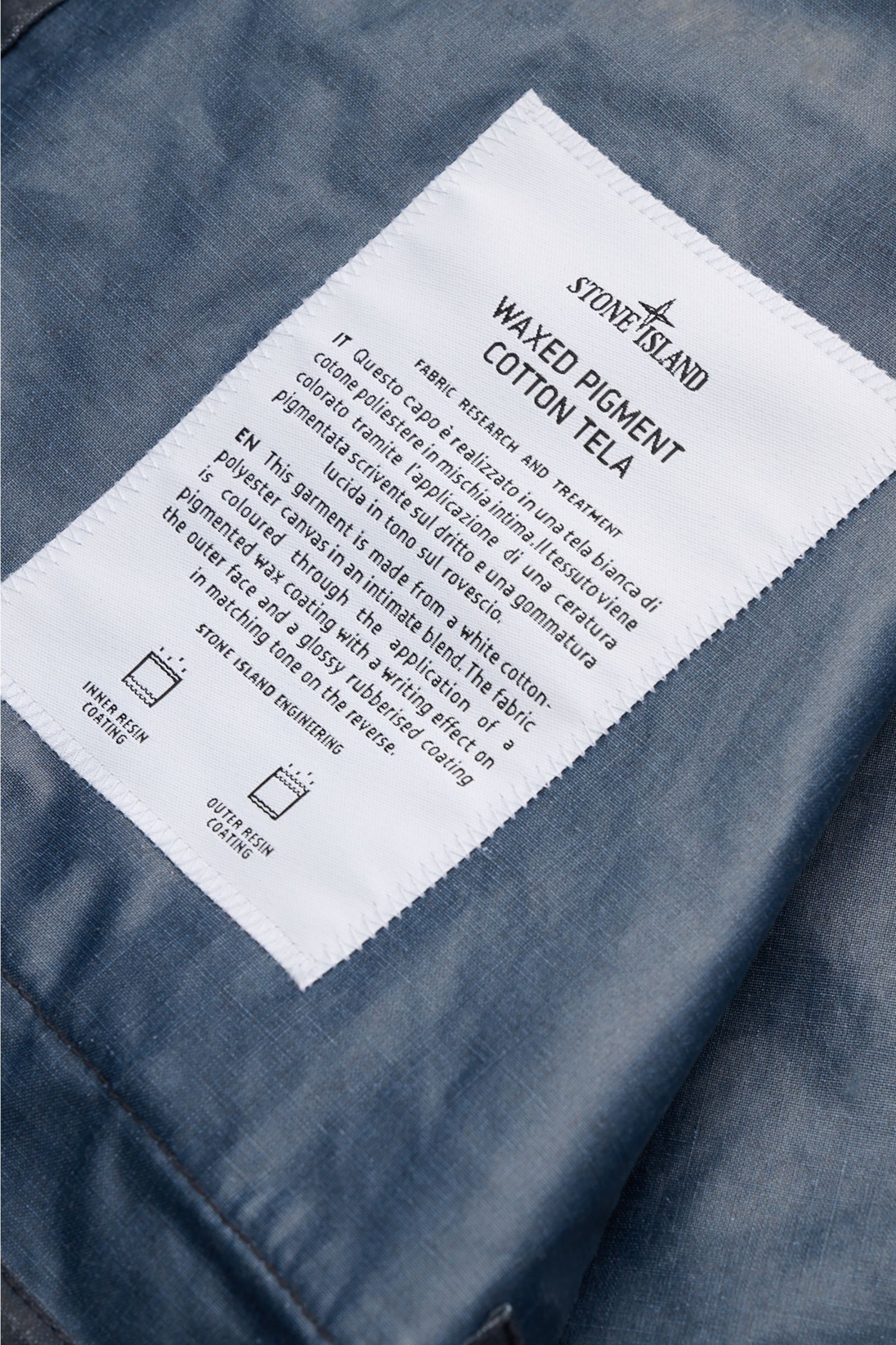 Close-up of the white fabric label inside Stone Island Waxed jacket 'Waxed Pigment Cotton Tela' navy, showing fabric details from a top-down perspective.

The waxed jacket 'Waxed Pigment Cotton Tela' by STONE ISLAND features the expected level of innov