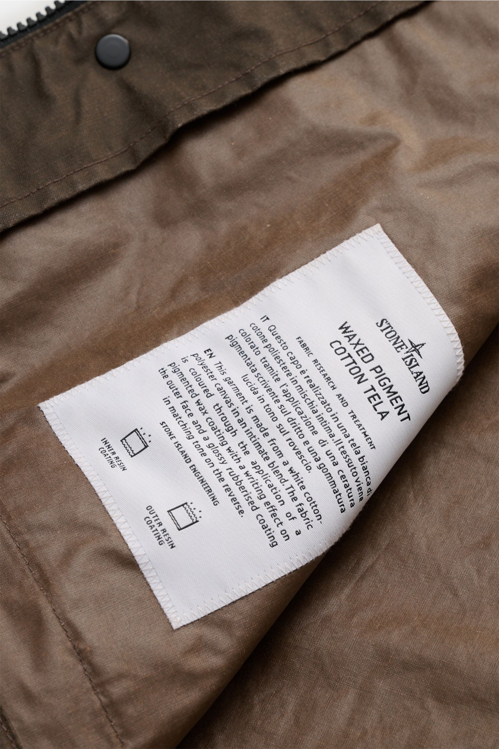 Stone Island Wachsjacke 'Waxed Pigment Cotton Tela' khaki, Nahaufnahme des Innenstoffs mit Pflegeetikett, robust, gewachst, wasserabweisend.