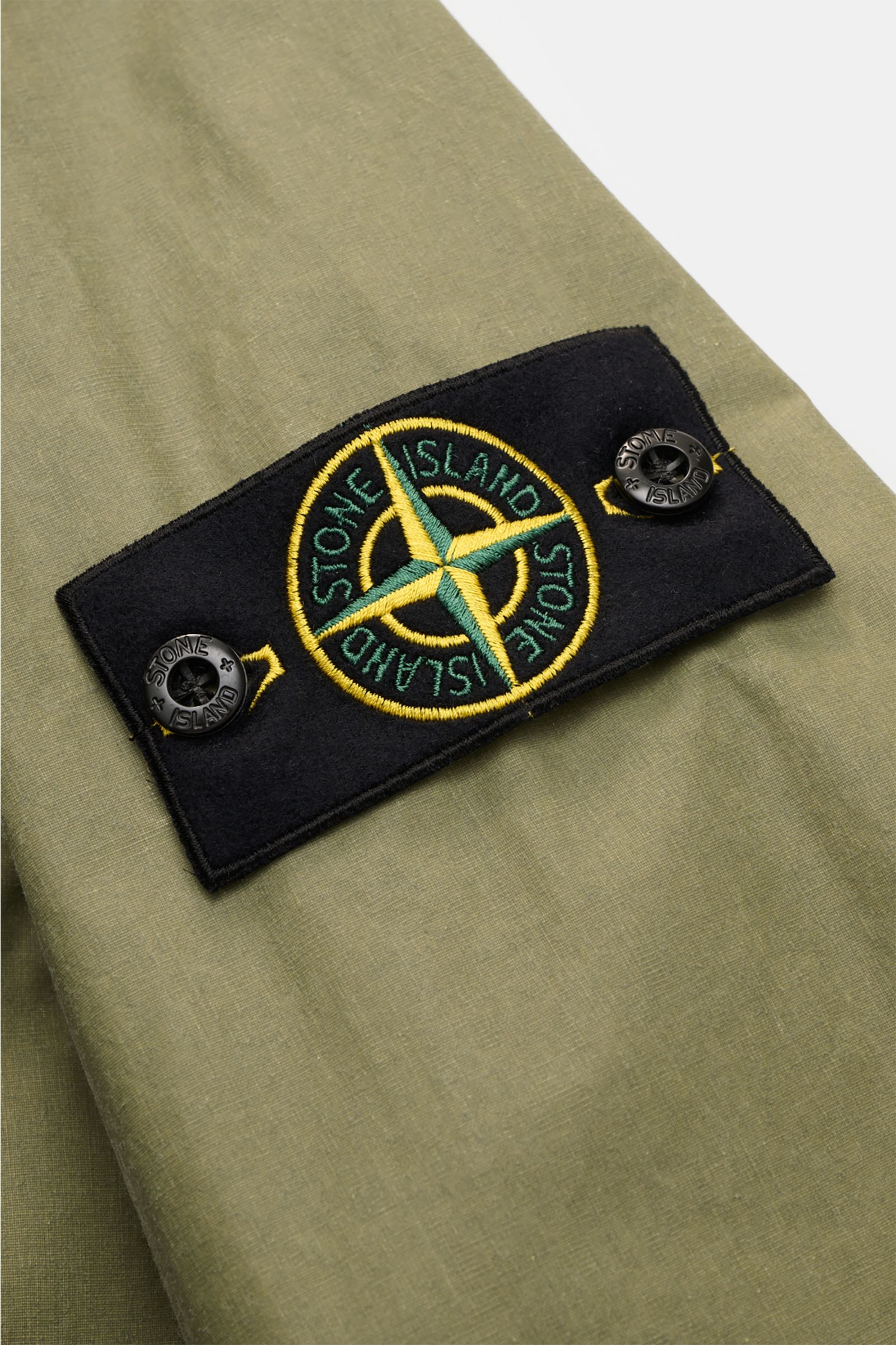 Close-up front view of the Stone Island Wachsjacke 'Waxed Pigment Cotton Tela' oliv showing the typical compass badge on olive waxed cotton fabric.

Description: Innovativ wie gewohnt und prädestiniert für unbeständiges Wetter ist die Wachsjacke 'Waxed Pi