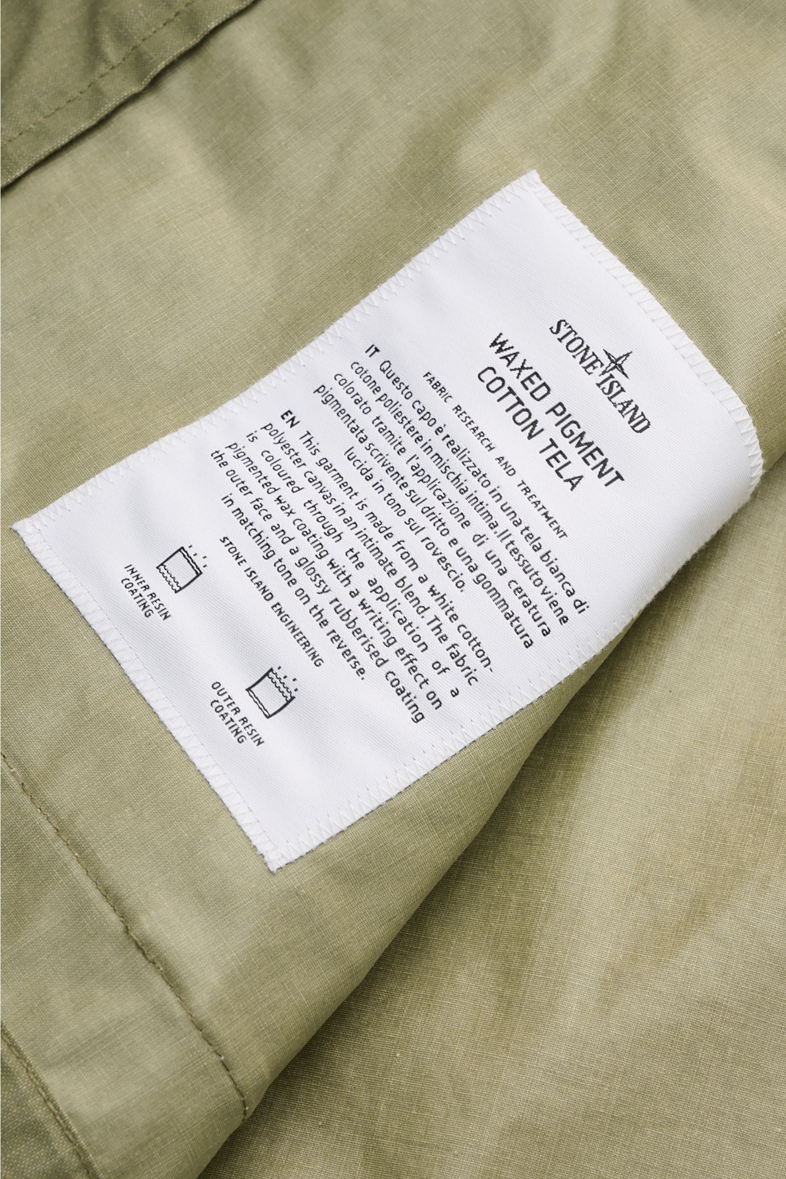 Close-up view of the inner label on the olive Stone Island Wachsjacke 'Waxed Pigment Cotton Tela', showing fabric details and stitching. Innovativ wie gewohnt und prädestiniert für unbeständiges Wetter ist die Wachsjacke 'Waxed Pigment Cotton Tela' von ST