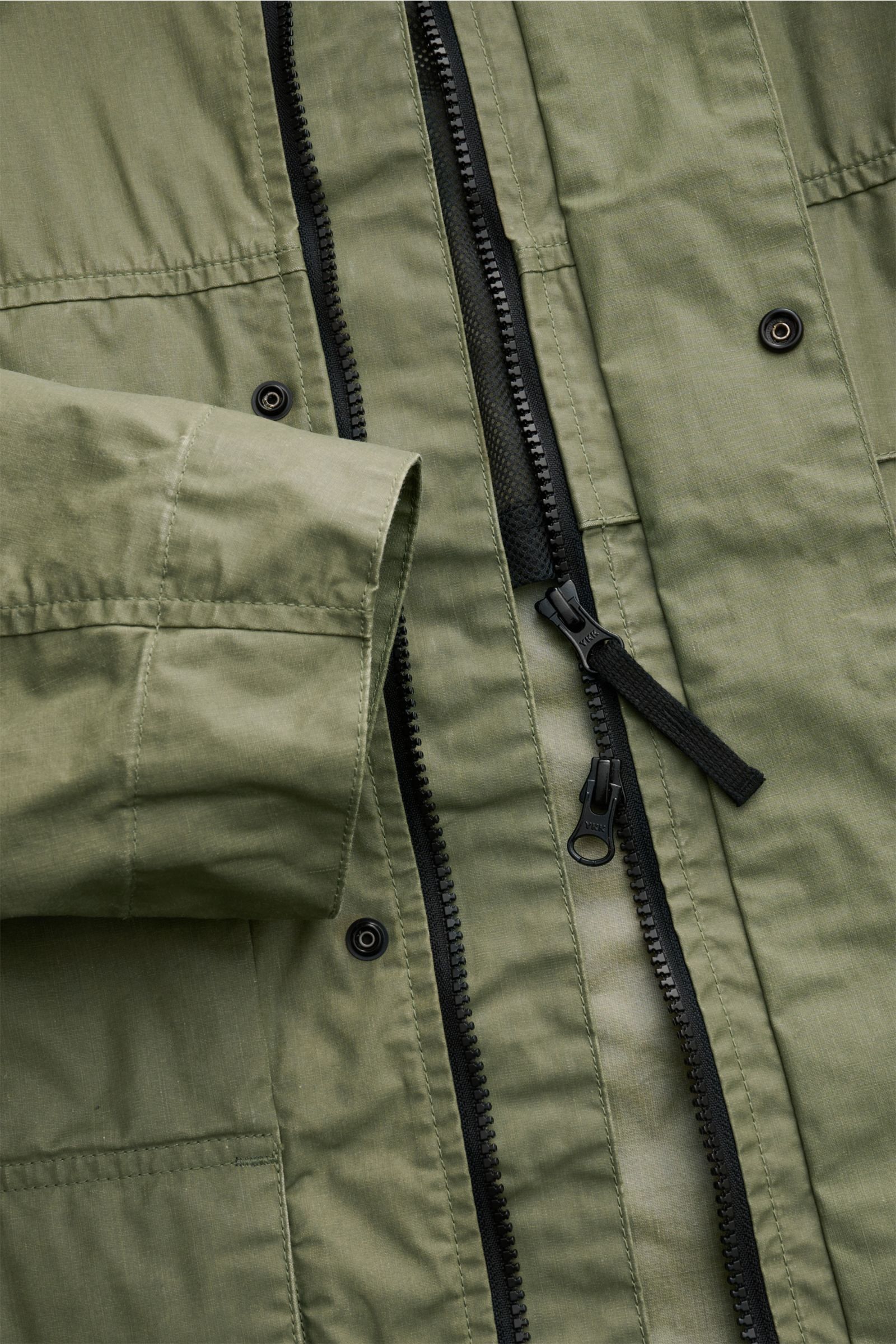 Stone Island Wachsjacke 'Waxed Pigment Cotton Tela' oliv, Nahaufnahme von innen mit robustem Zwei-Wege-Reißverschluss, gewachstem Baumwollstoff und Druckknöpfen.