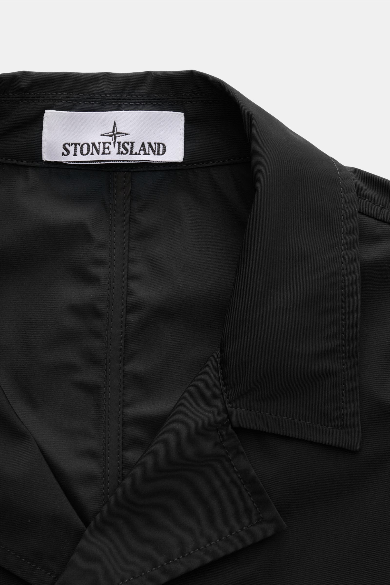 Close-up front view of the collar and label of the Stone Island Jacke 'Micro Twill' schwarz, made of smooth, high-quality microfiber fabric. Eleganz trifft Funktion: Die STONE ISLAND Jacke überzeugt mit Micro-Twill in glatter, angenehmer Haptik und wird m
