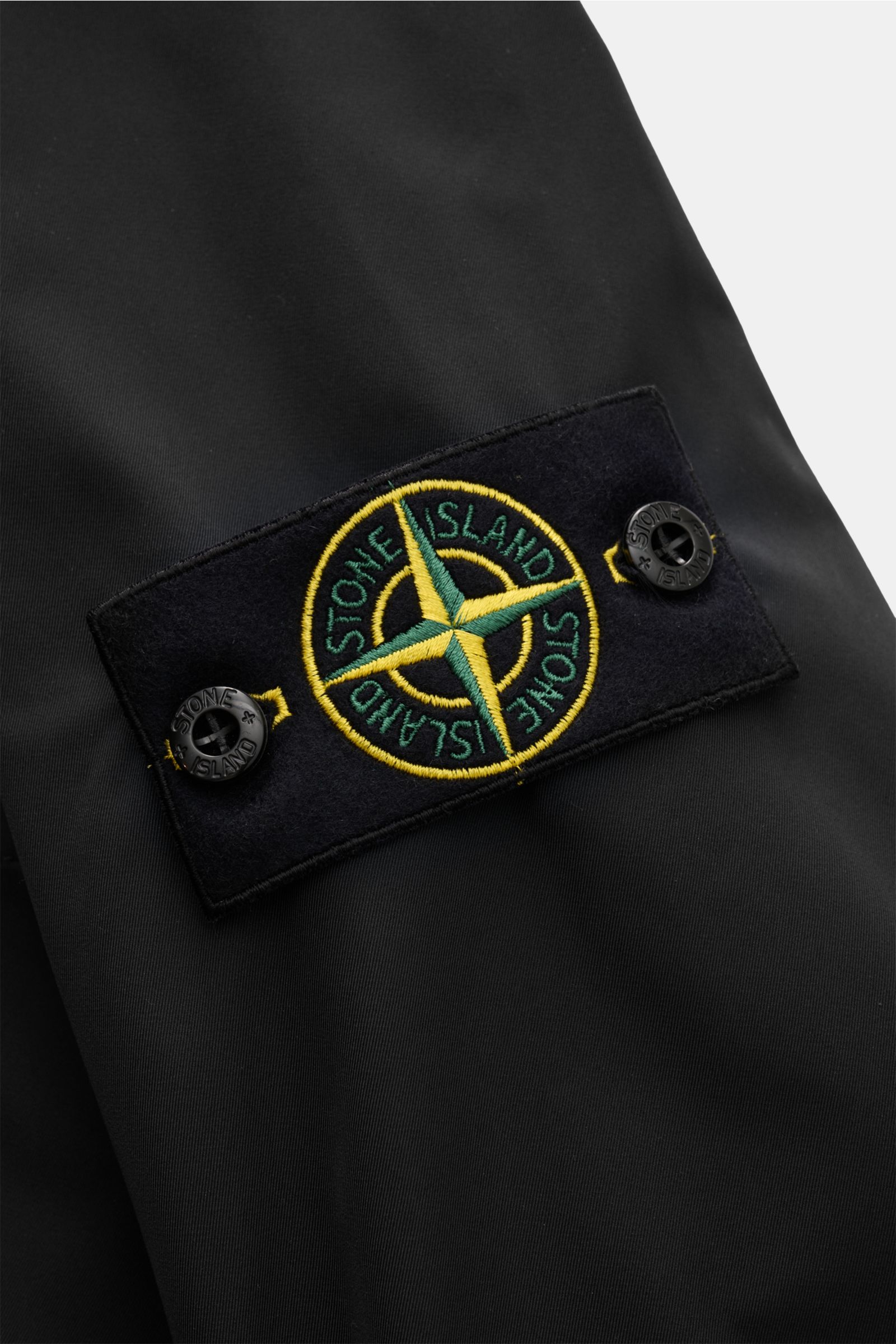 Close-up side view of the Stone Island Jacke 'Micro Twill' schwarz showing the black microfibre fabric with the signature compass badge on the upper arm, highlighting its smooth, water-repellent finish and high-quality design.

Eleganz trifft Funktion: