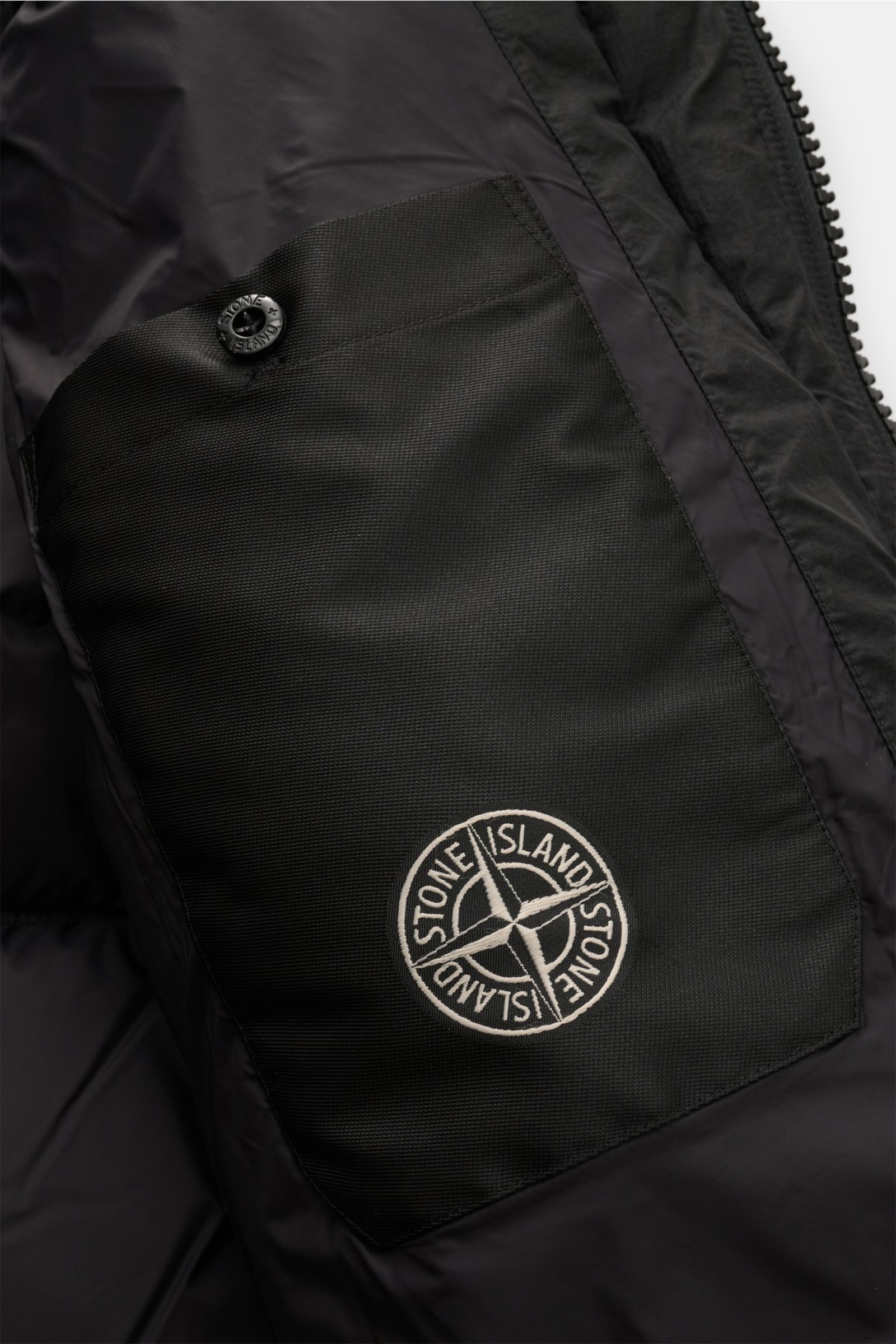 Close-up interior view of Stone Island Down jacket 'Seam Faded Light Nylon Tela' black showing branded inner pocket with button detail, smooth lining.

Stay in style even on cold days: This down jacket by STONE ISLAND has a warm down lining that makes 