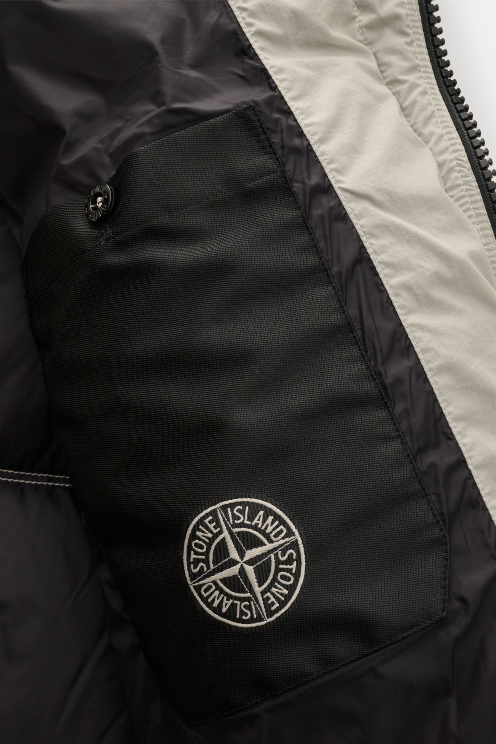 Nahaufnahme der Innentasche mit Stone Island Logo der offwhite Stone Island Daunenjacke 'Seam Faded Light Nylon Tela' aus hochwertiger Microfaser.