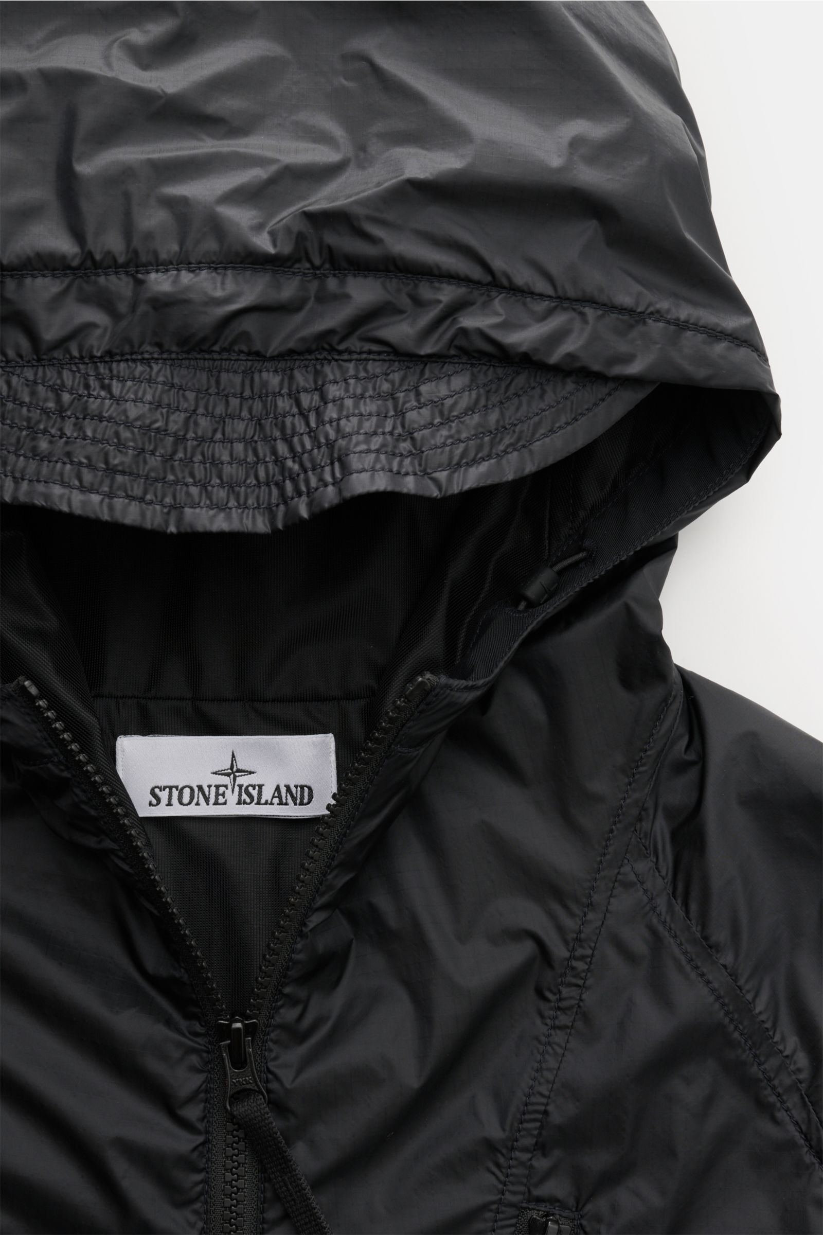 Close-up front view of the Stone Island Blouson 'Light Ripstop Cordura' black, showing the hood, zipper, and fabric details. Robust yet lightweight: This blouson by STONE ISLAND is made of high-strength ripstop fabric known for durability with a special f